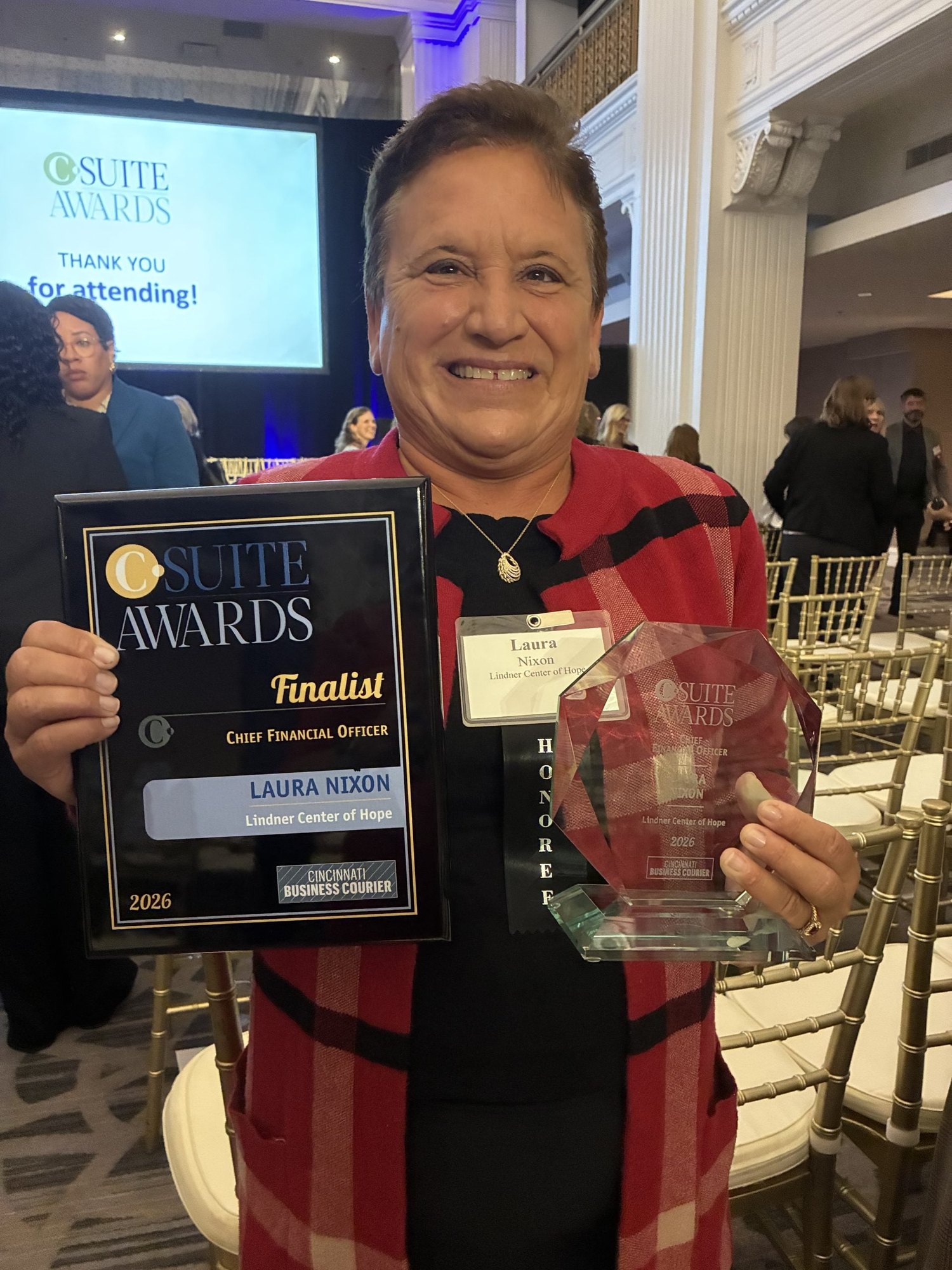 A woman smiles while holding an award plaque and glass trophy at a banquet ceremony.