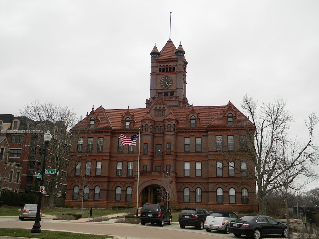 Multi-story red-brick building with a prominent clock tower and an American flag out front.