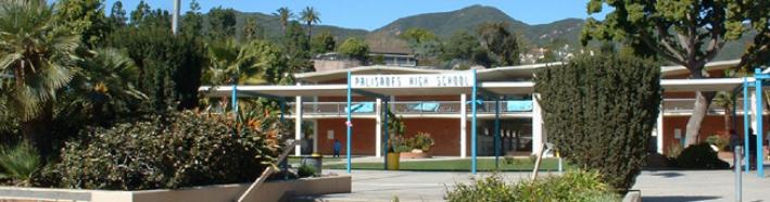 Low-rise school building with covered walkway, palm trees, and hills behind it.