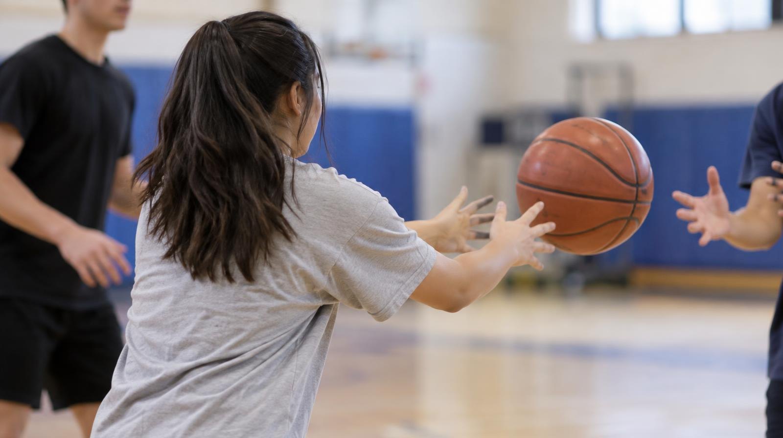 Students passing a ball in a circle inside a bright school gymnasium.
