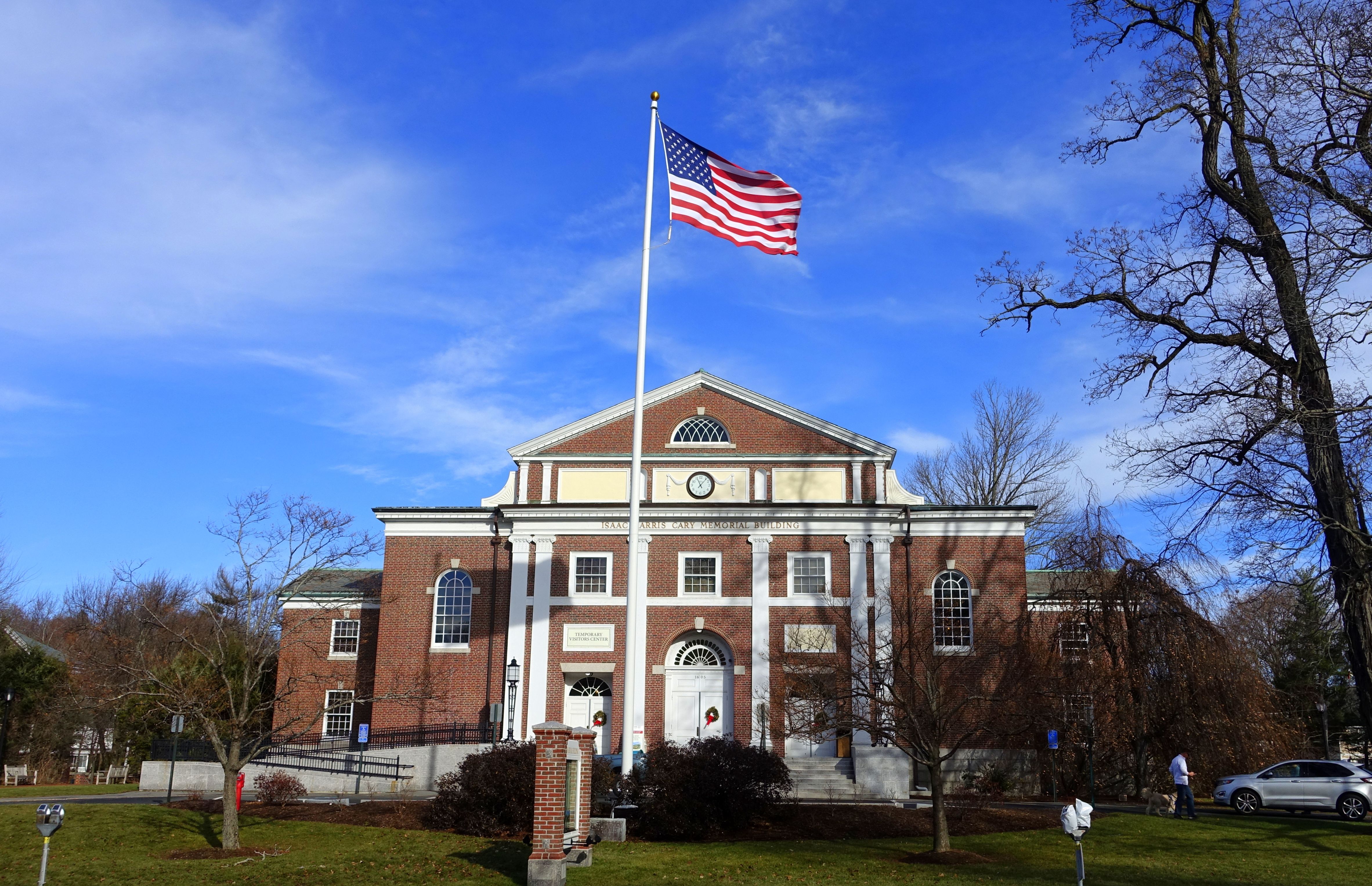 Brick neoclassical building with flagpole flying the American flag, bare trees, blue sky.