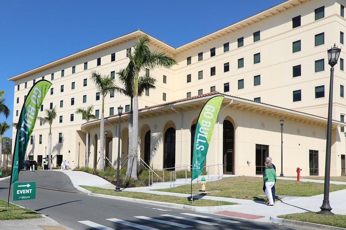 Multi-story cream-colored academic building with palm trees and green Go Bulls banners out front.