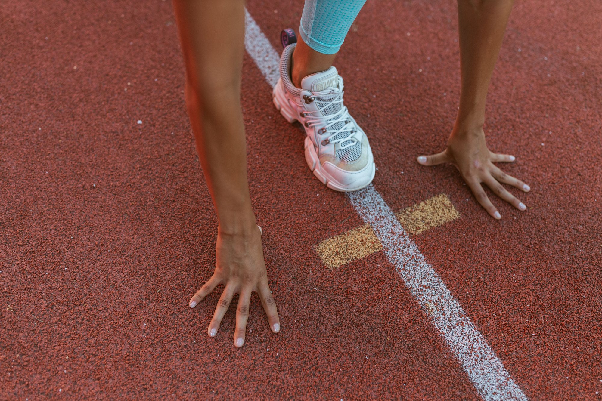 Close-up of an athlete's hands and foot ready at the starting line on a running track.