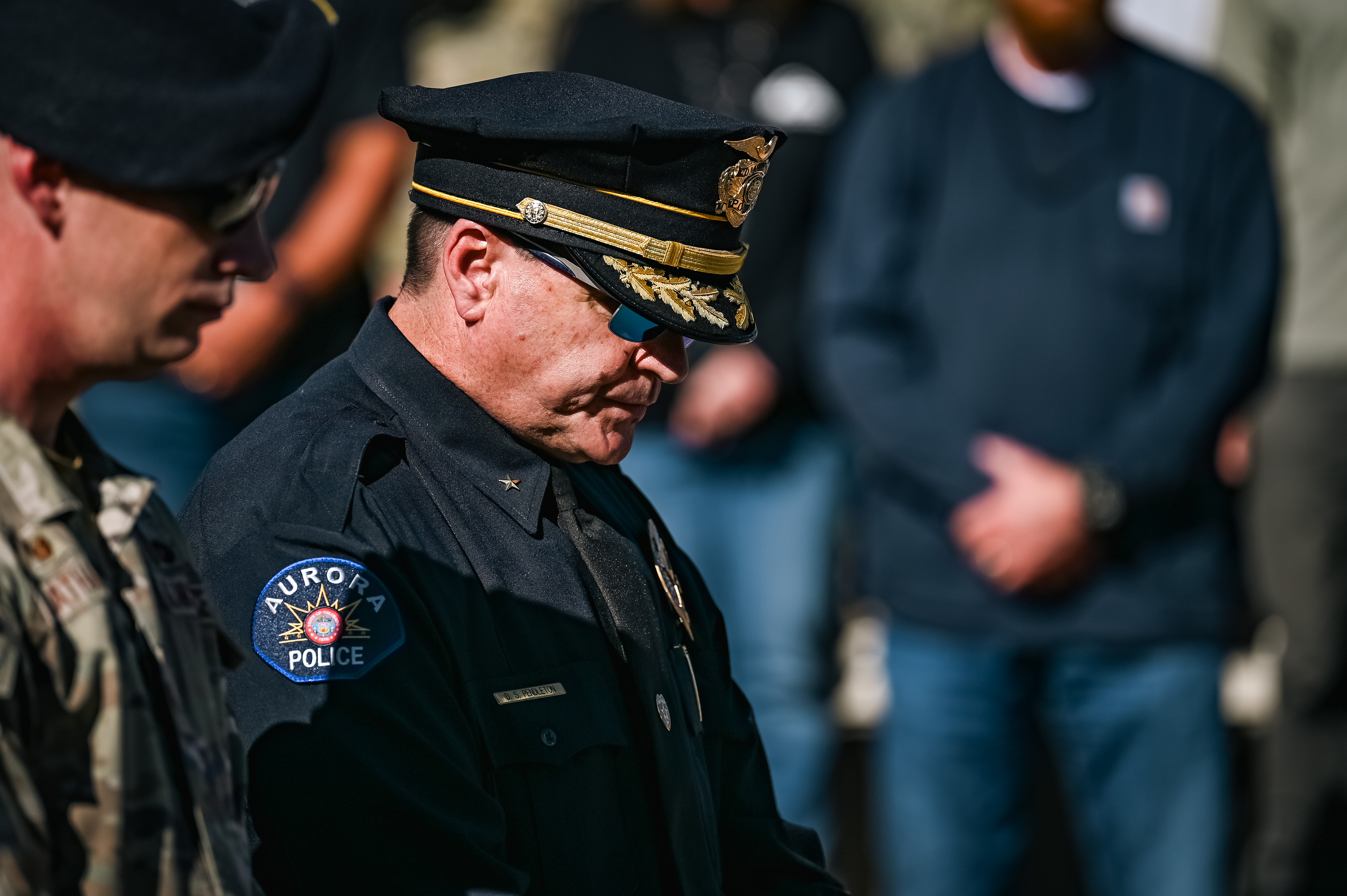 A uniformed police officer bows his head during a moment of silence outdoors.
