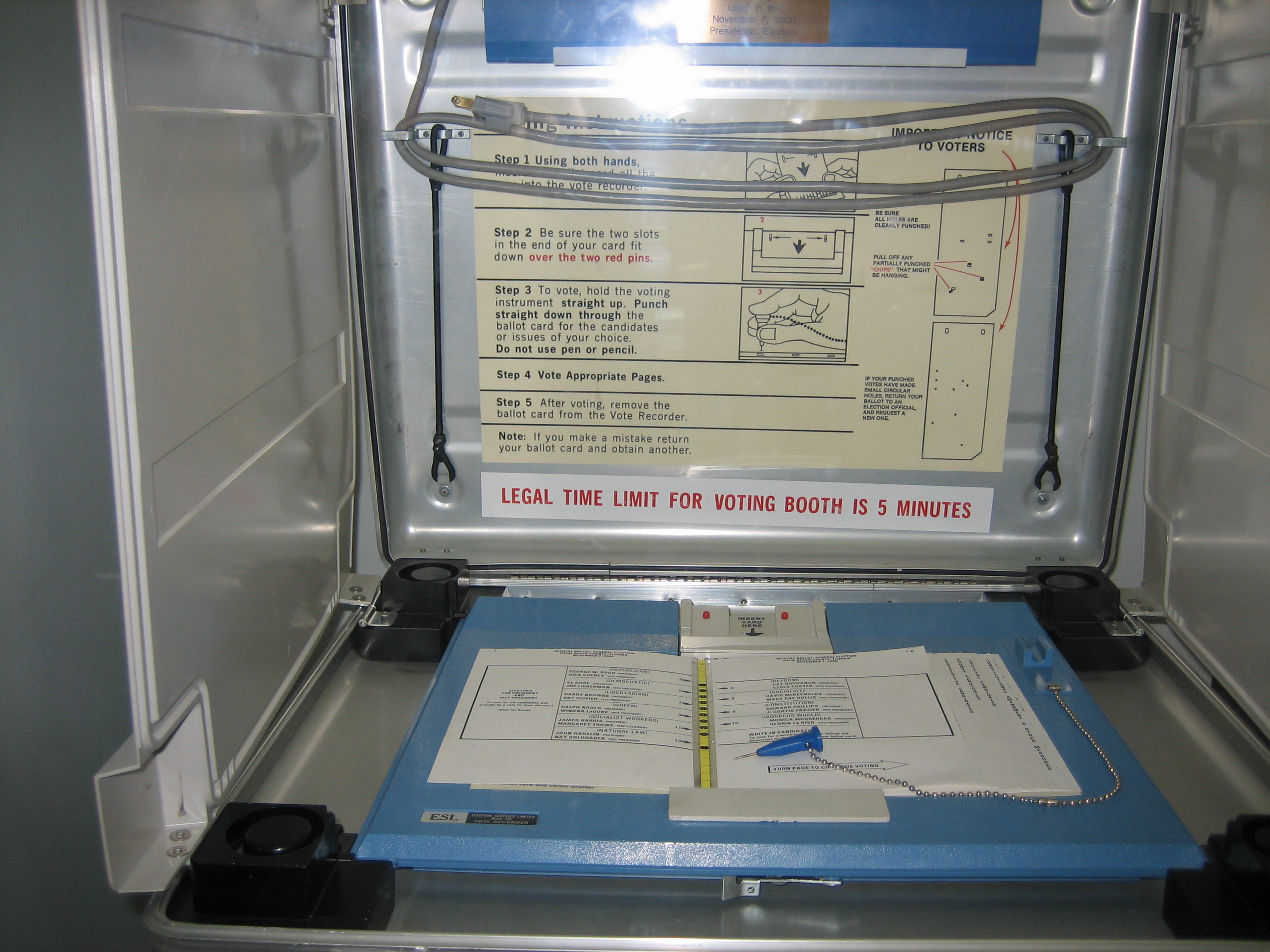 Inside a voting booth showing a ballot card, pen, and posted voting instructions.