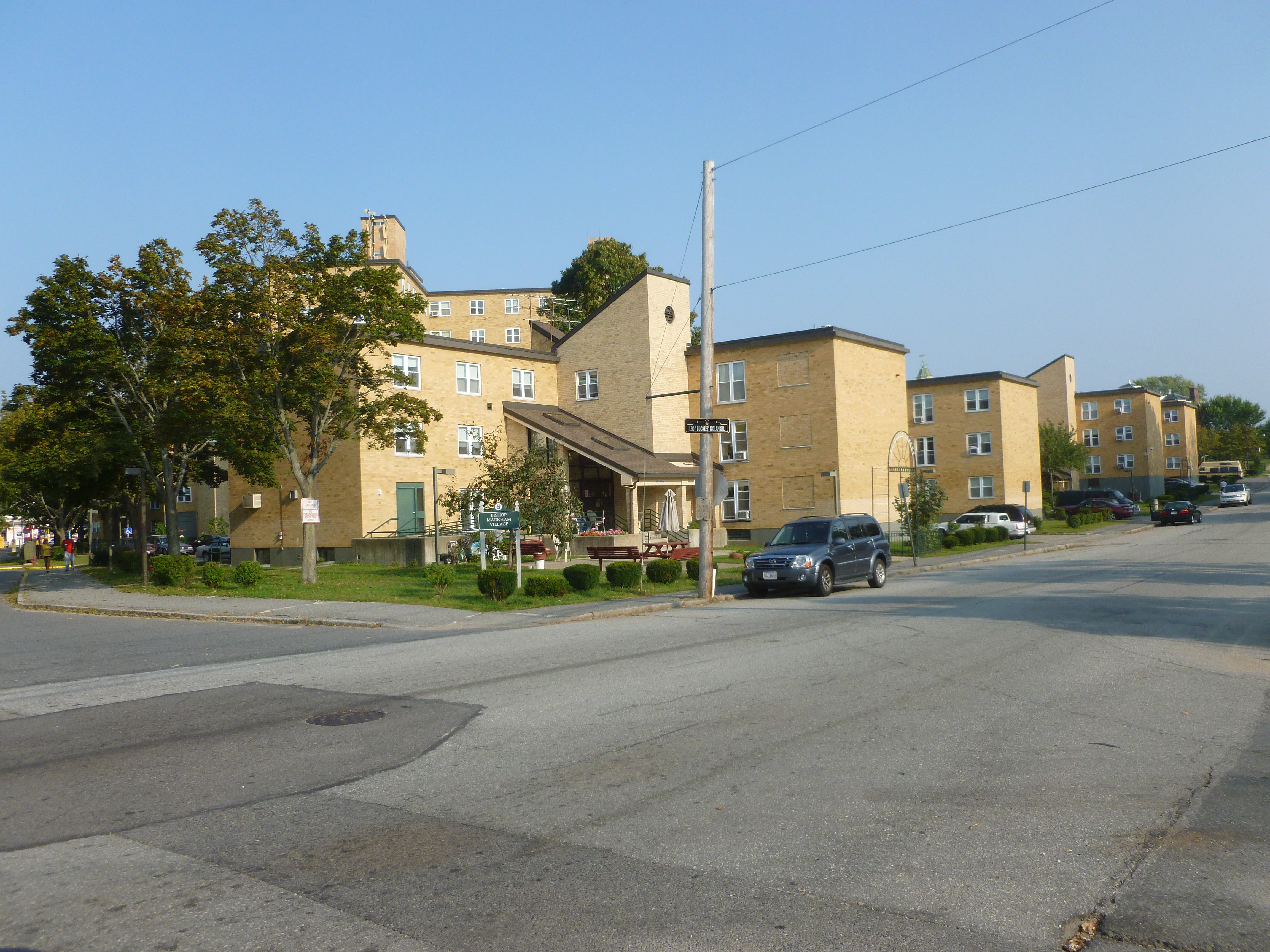 Multi-story brick affordable housing apartment buildings along a street with parked cars.