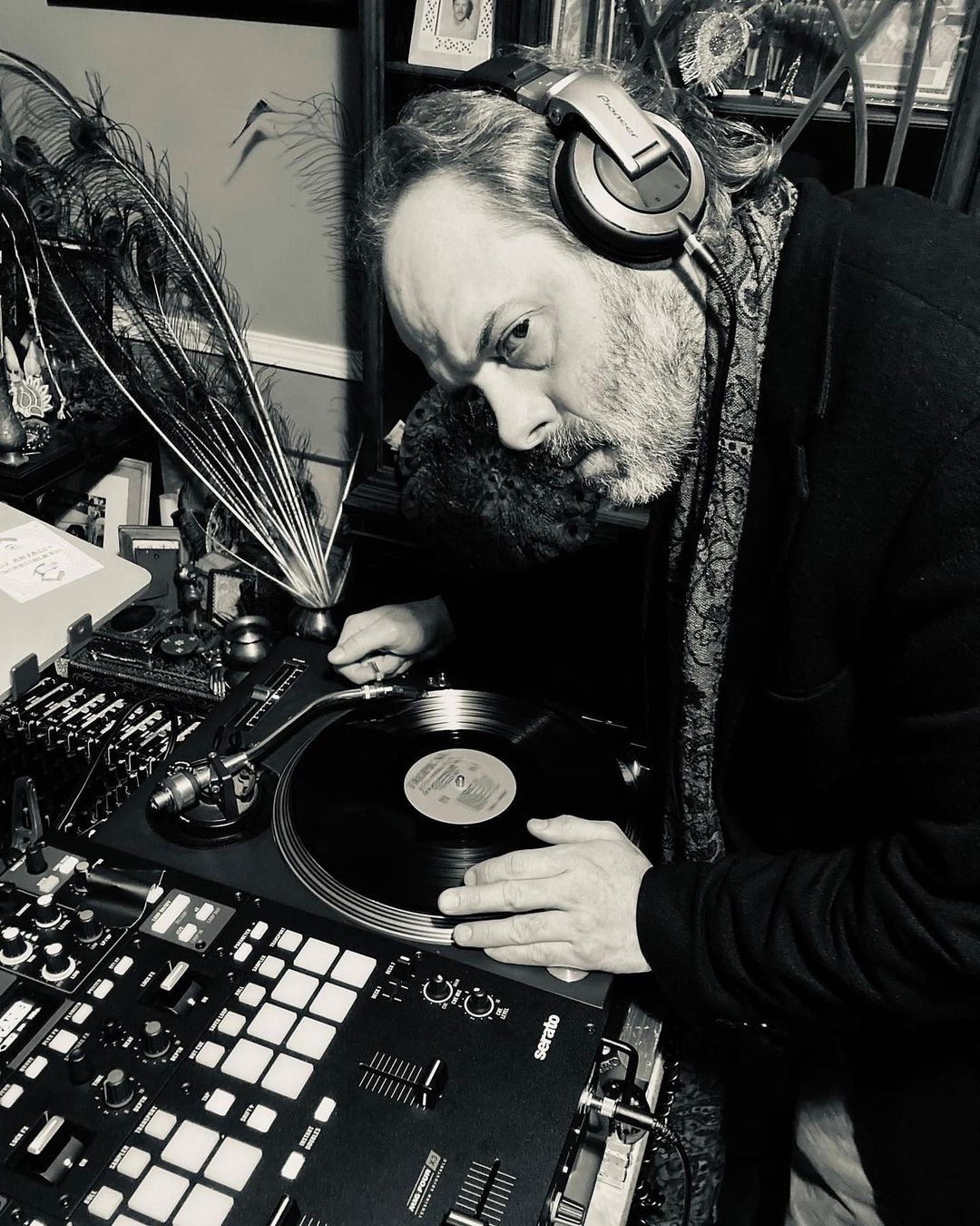 A man with headphones handles a vinyl record on a turntable at a DJ setup.