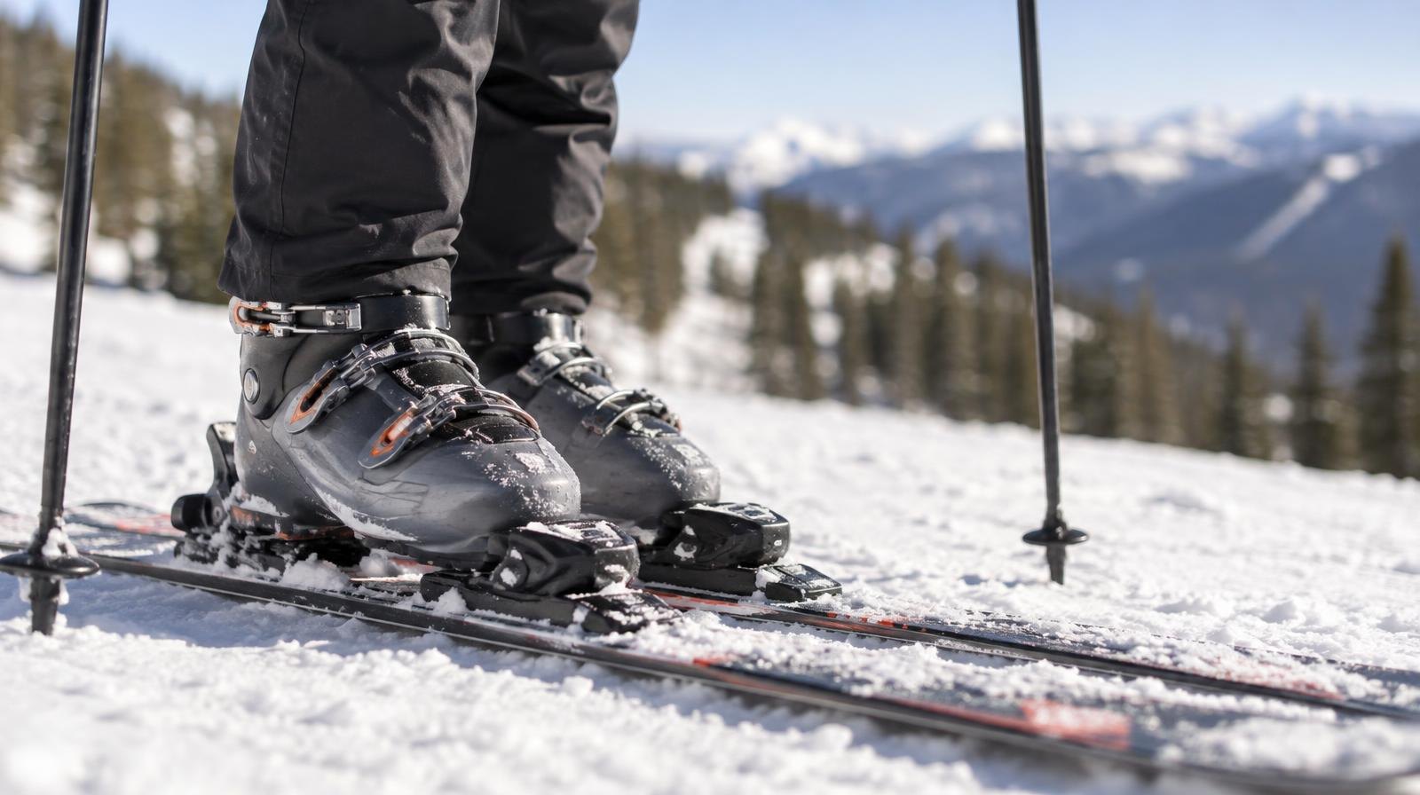 Alpine ski boots clipped into skis resting on packed snow with poles nearby.