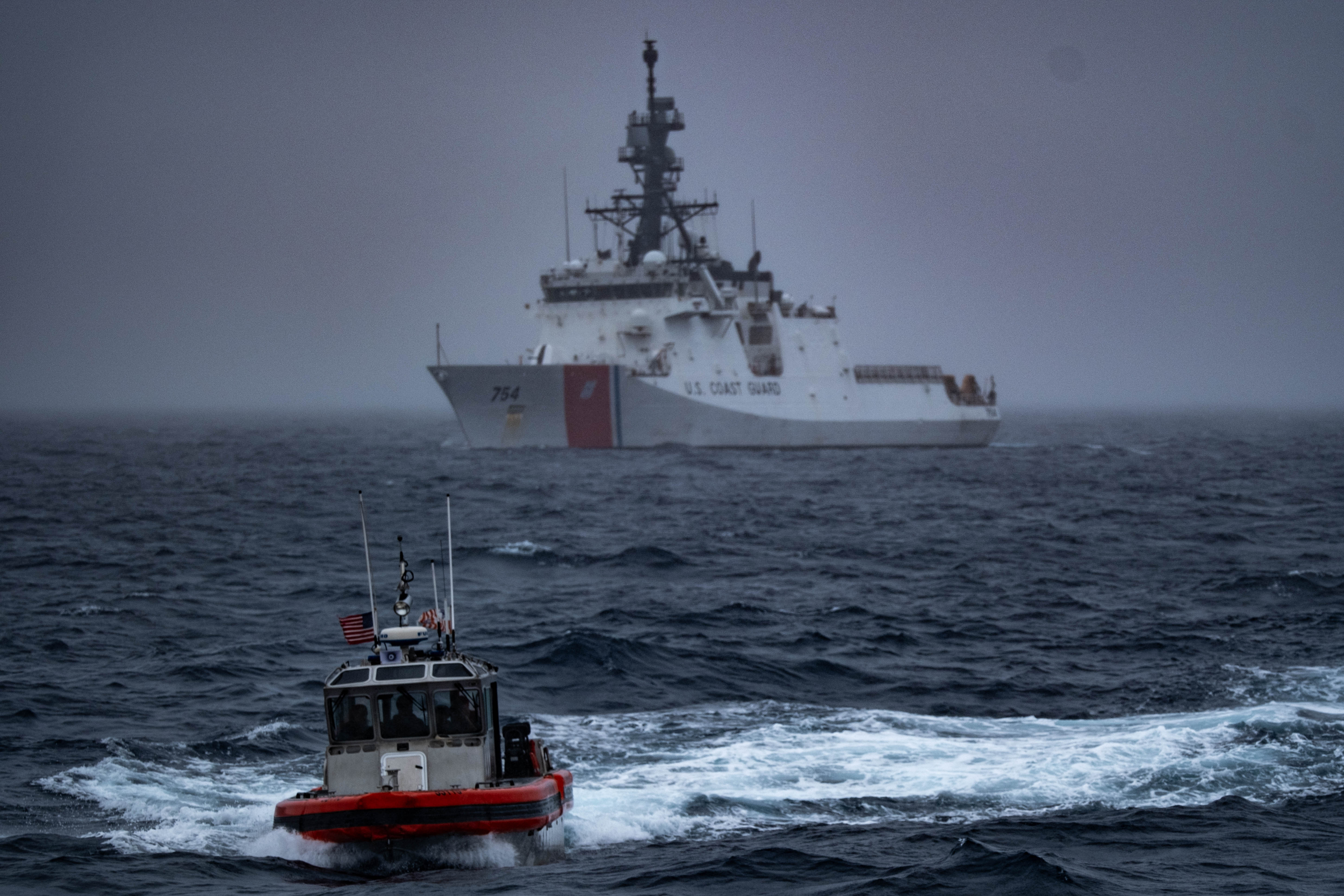 A large white Coast Guard cutter and a smaller orange patrol boat at sea.