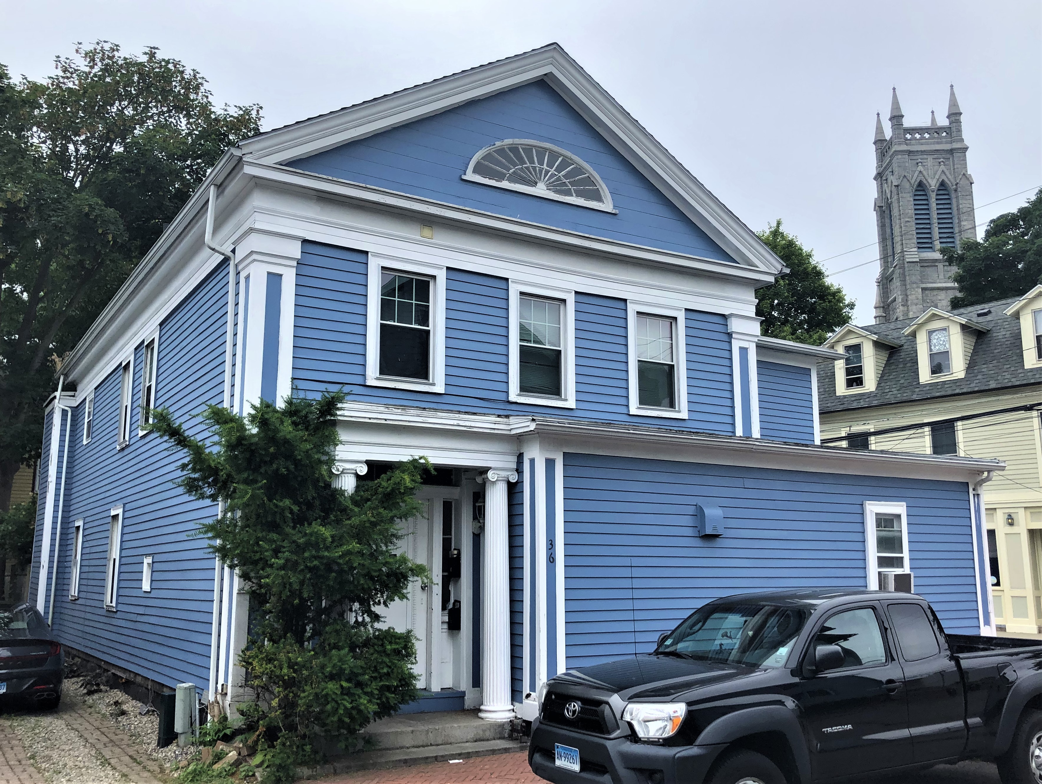 Two-story blue clapboard Greek Revival house with white pilasters and triangular pediment.