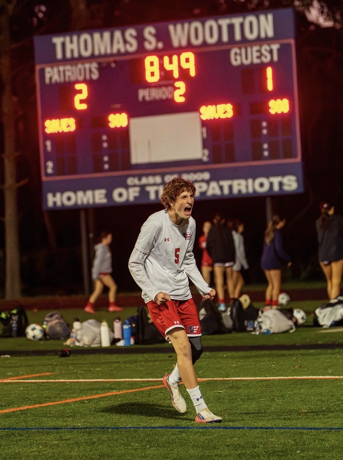 Soccer player in white and red uniform celebrating on a lit field at night.