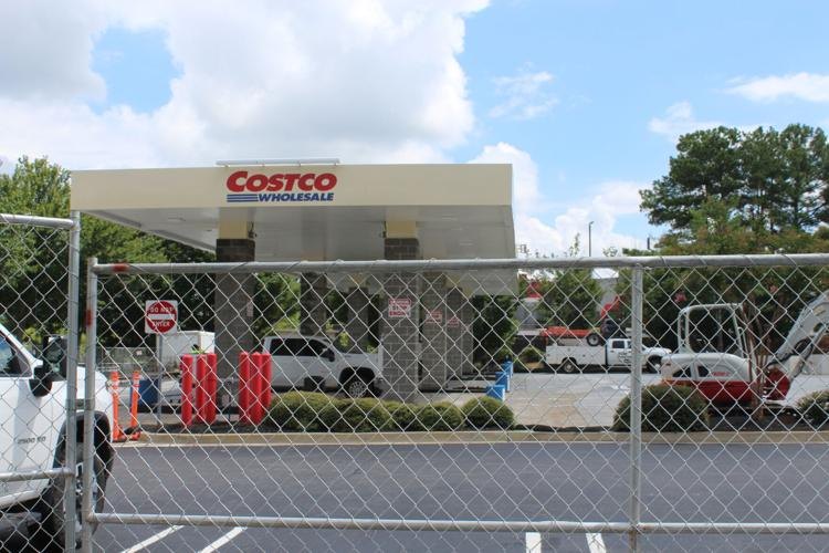 Chain-link construction fence in front of a Costco gas station with red pumps visible behind it.