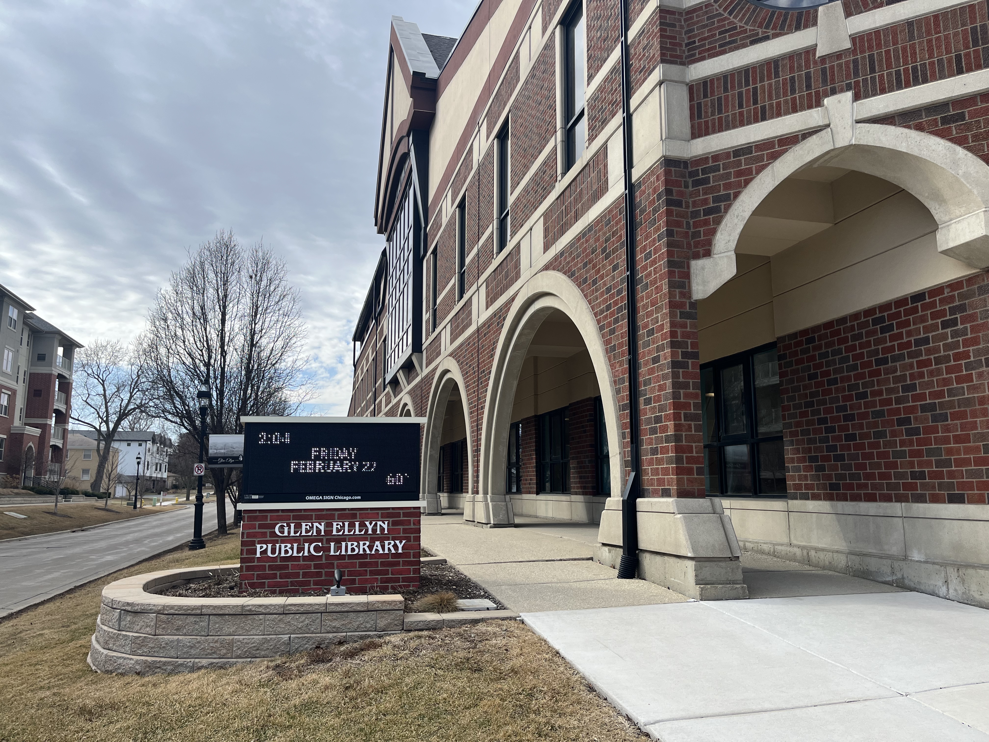 Exterior of a red-brick library building with arched entryways and a digital sign.