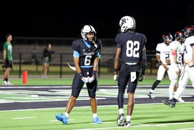 Two football players in dark blue uniforms on a lit field at night.