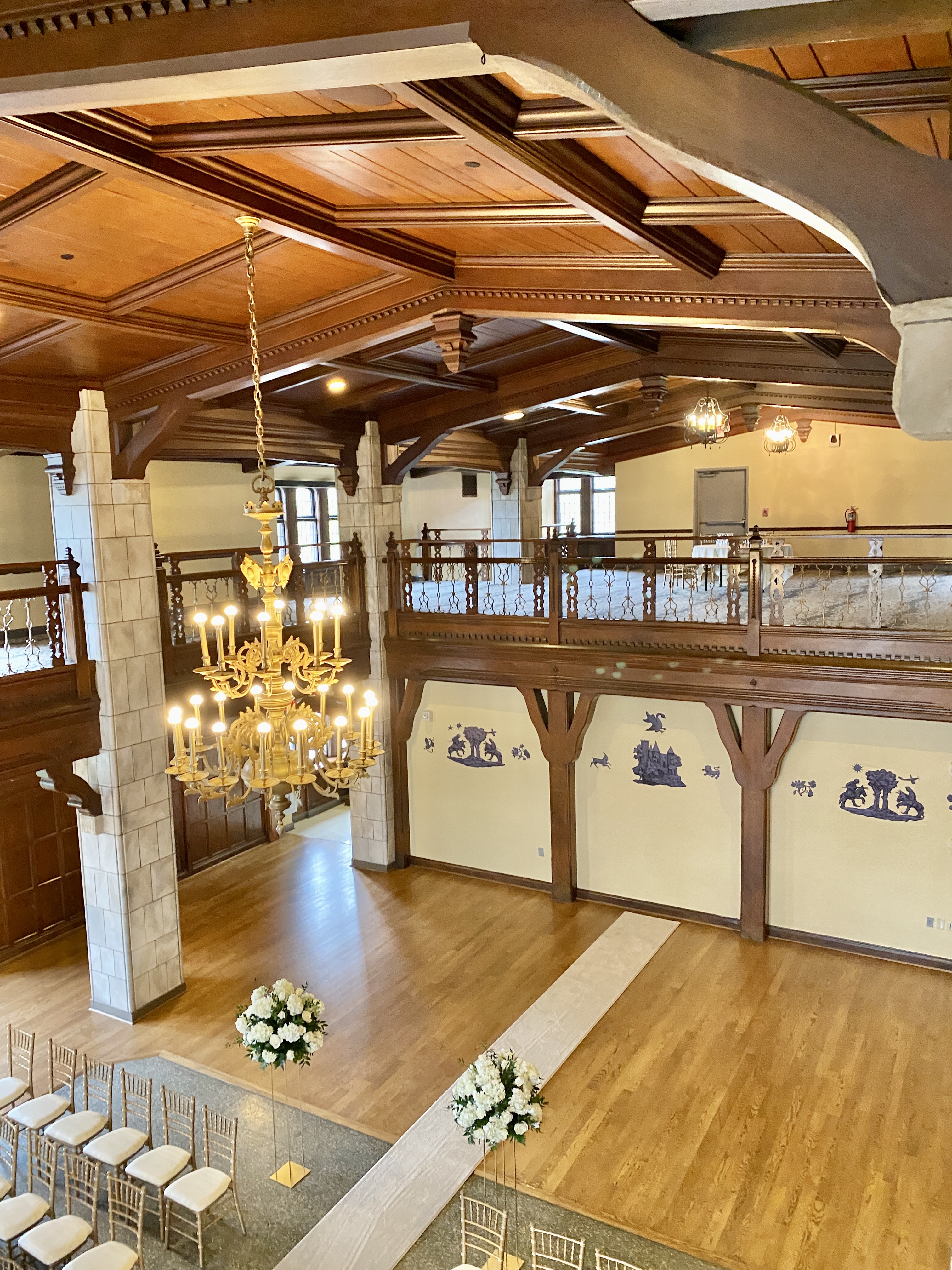 Ornate hotel ballroom with wooden coffered ceiling, chandelier, and rows of gold chairs.