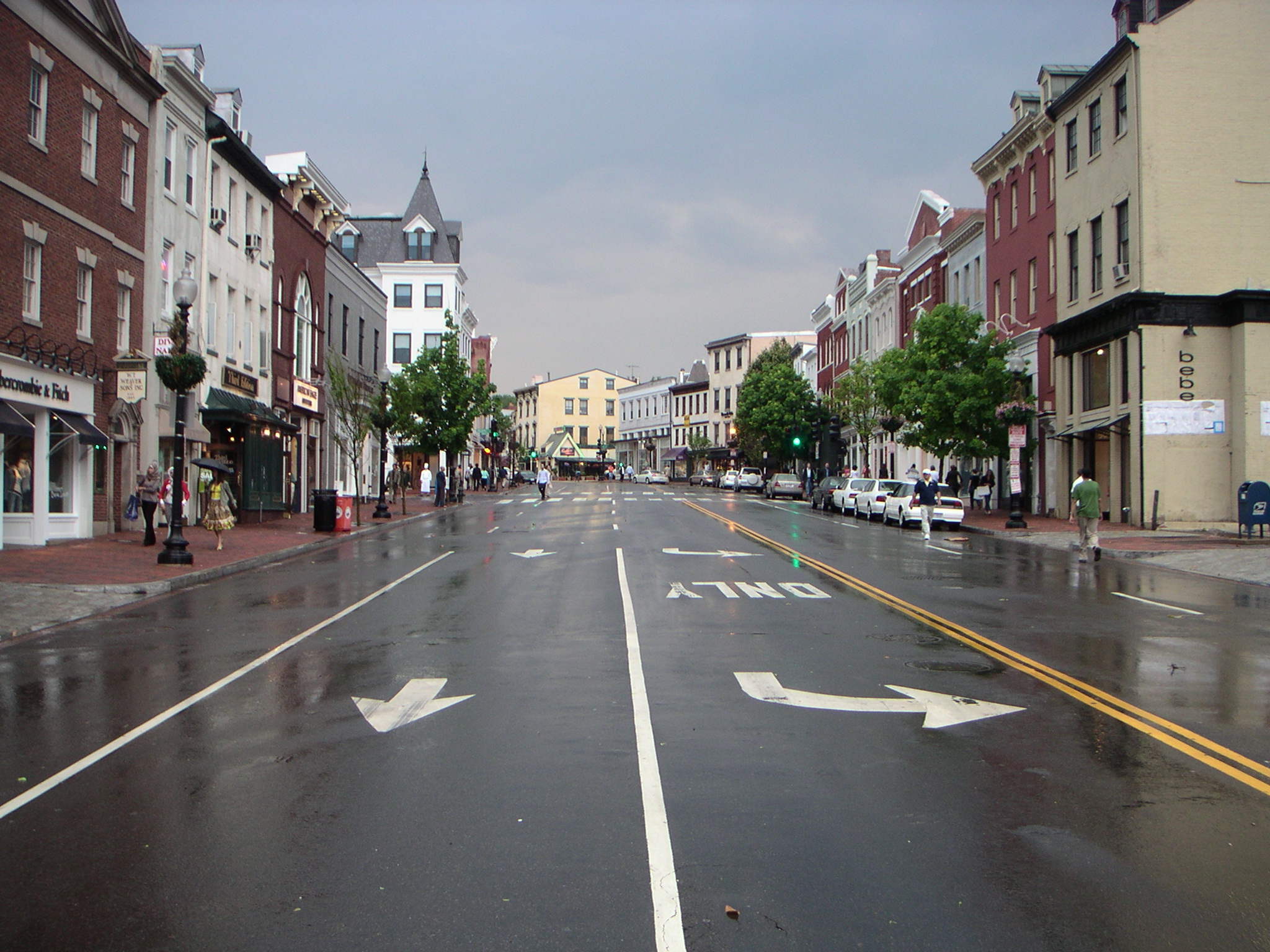 Rain-slicked Wisconsin Avenue NW lined with historic brick storefronts in Georgetown.