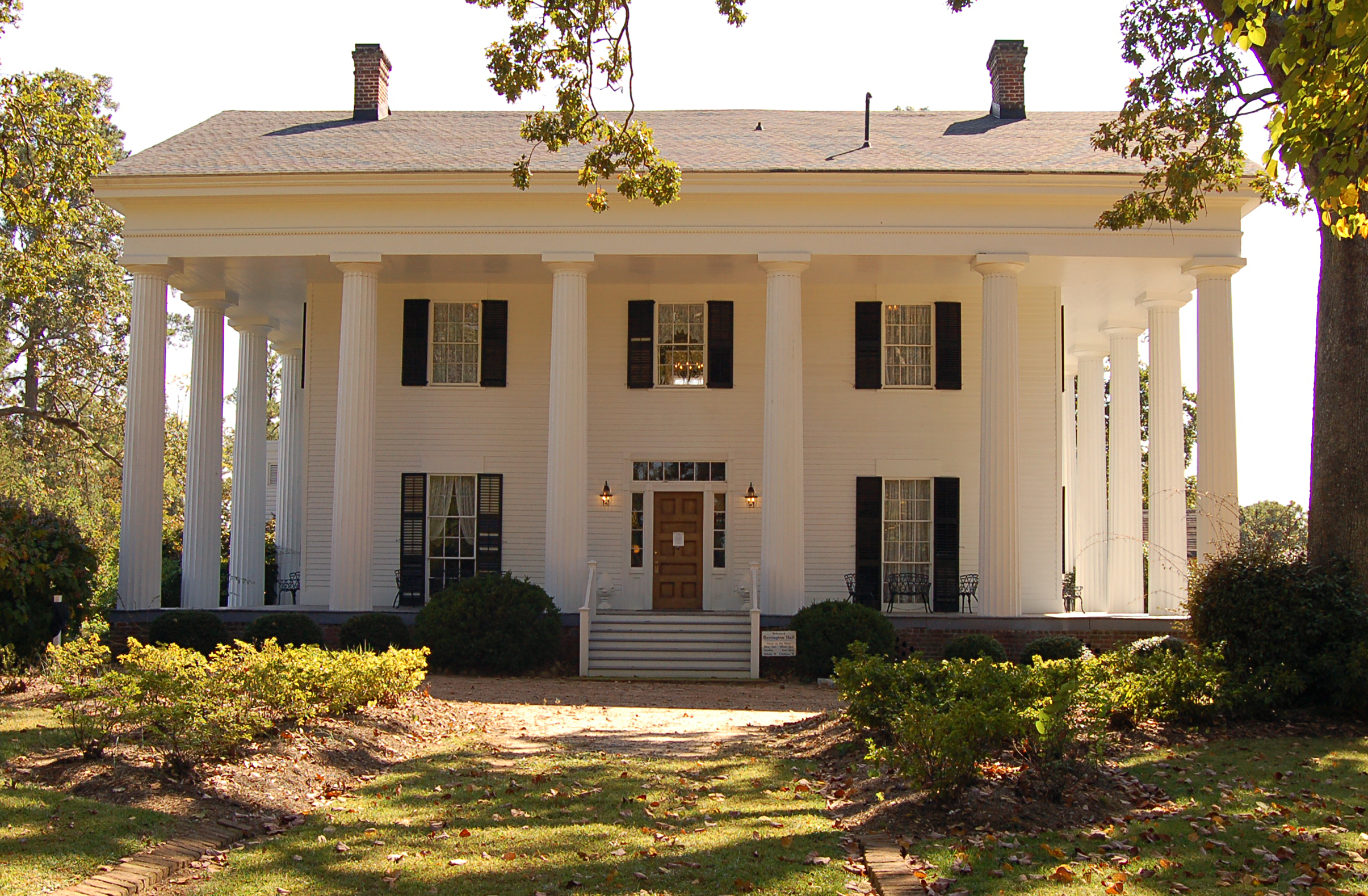 White two-story Greek Revival mansion with tall columns, black shutters, and a central entrance.