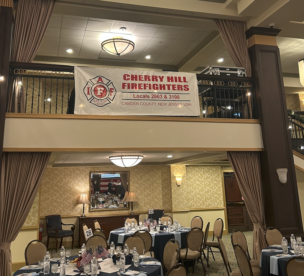 Banquet hall with round tables and a large banner reading Cherry Hill Firefighters Locals 2663 and 3198.