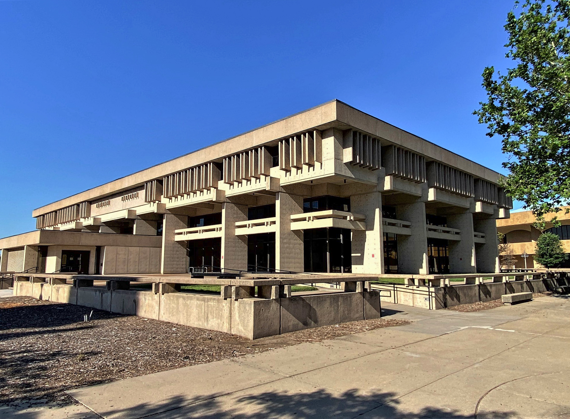 Exterior of a large brutalist concrete public library building under a clear blue sky.