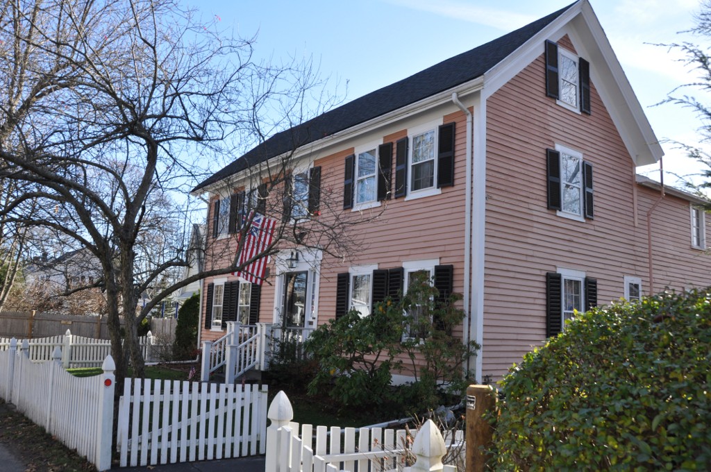 Two-story colonial house with pink siding, black shutters, and a white picket fence.