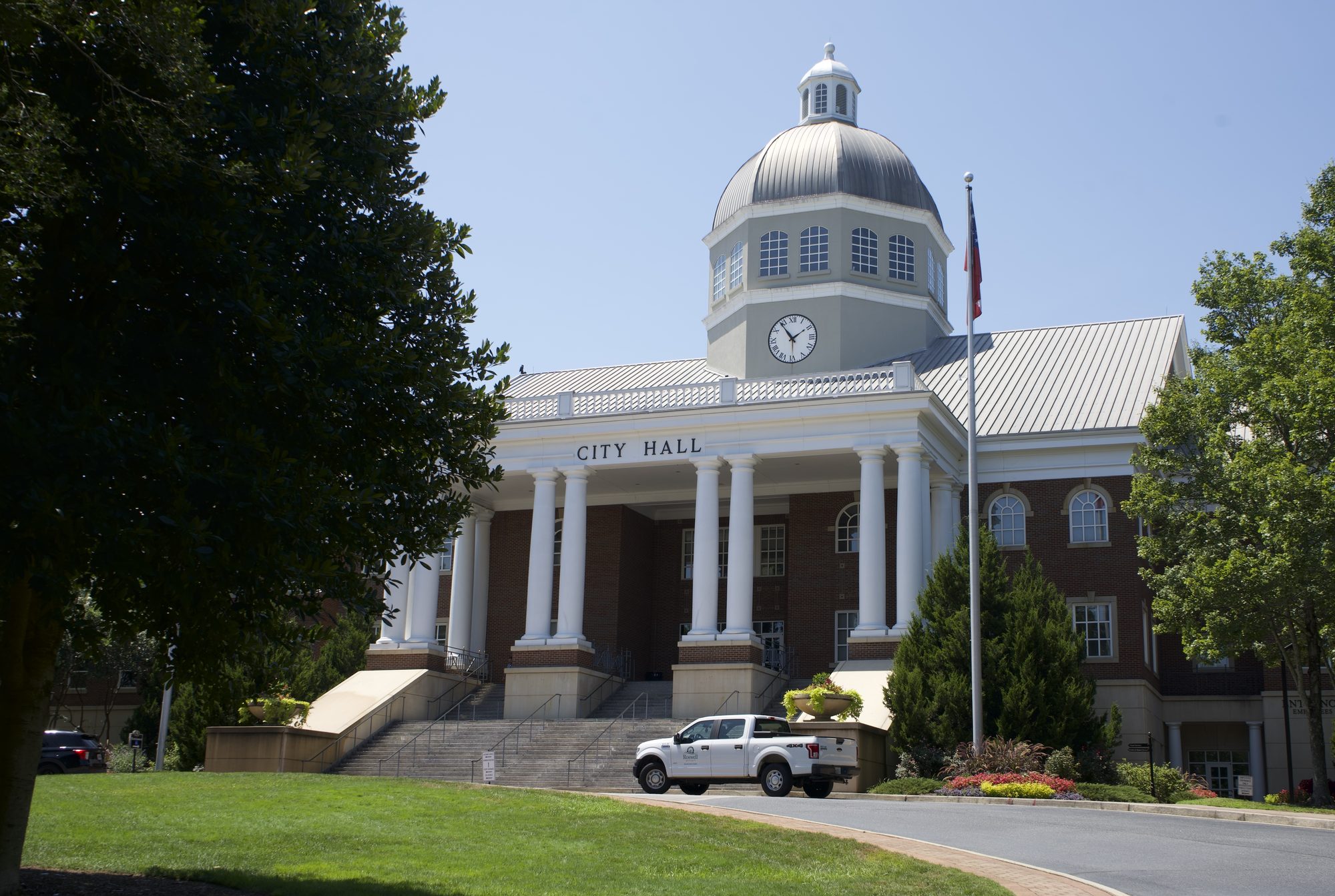 Two-story brick city hall with domed clock tower and white columned entrance.