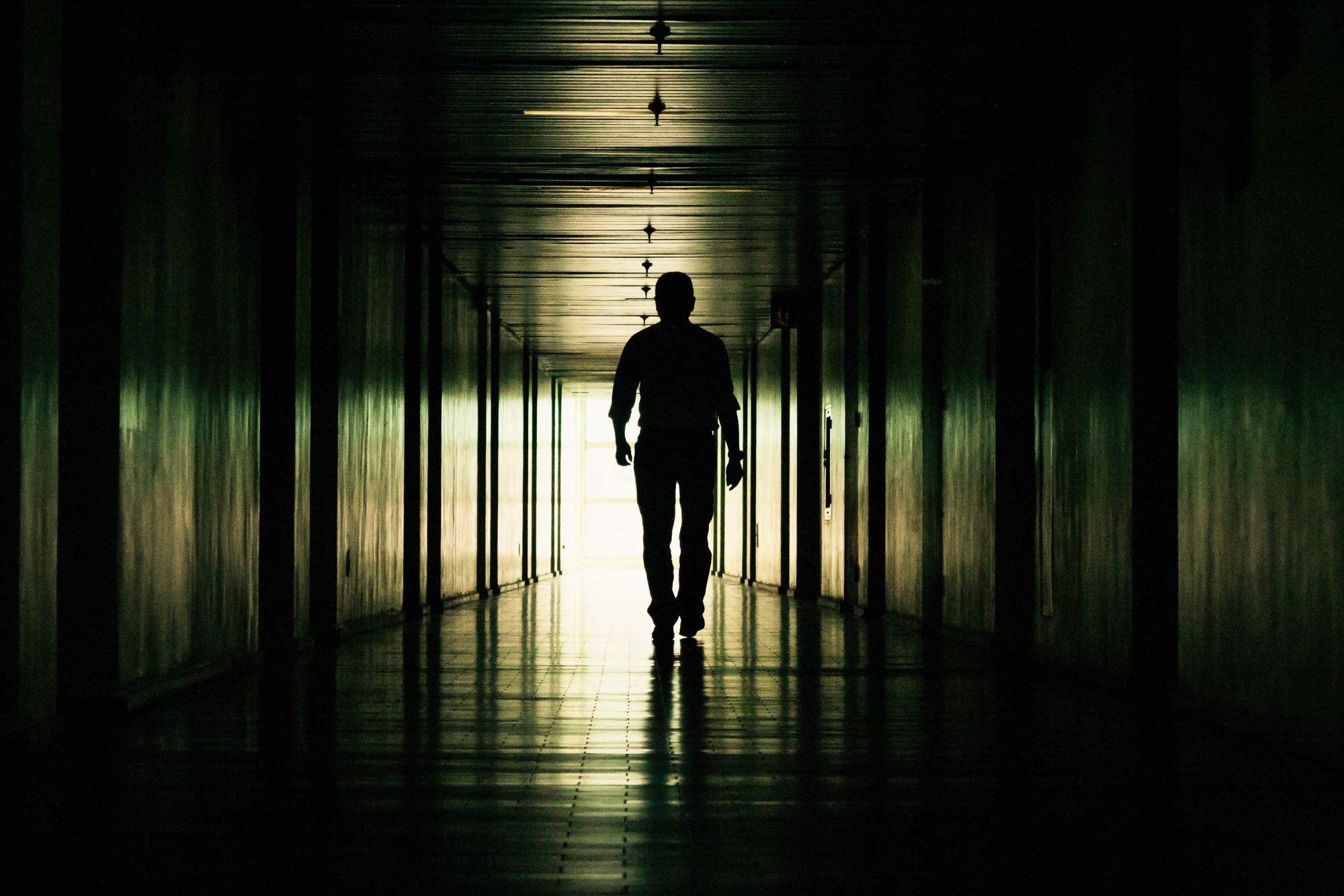 Shadowy silhouette of a person walking through a dark, dramatic hallway.