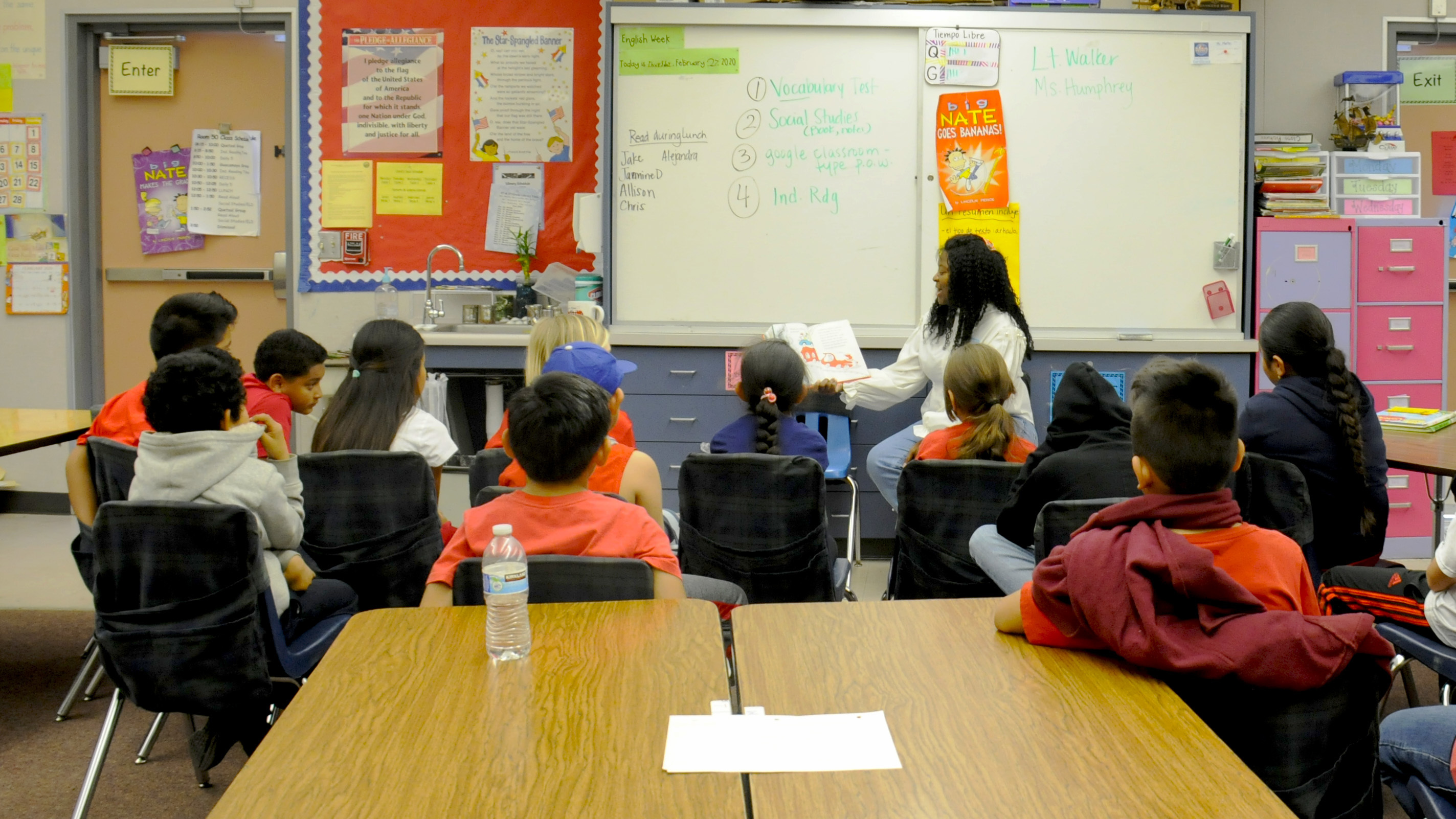 An adult reads a book aloud to elementary school students seated in a classroom.