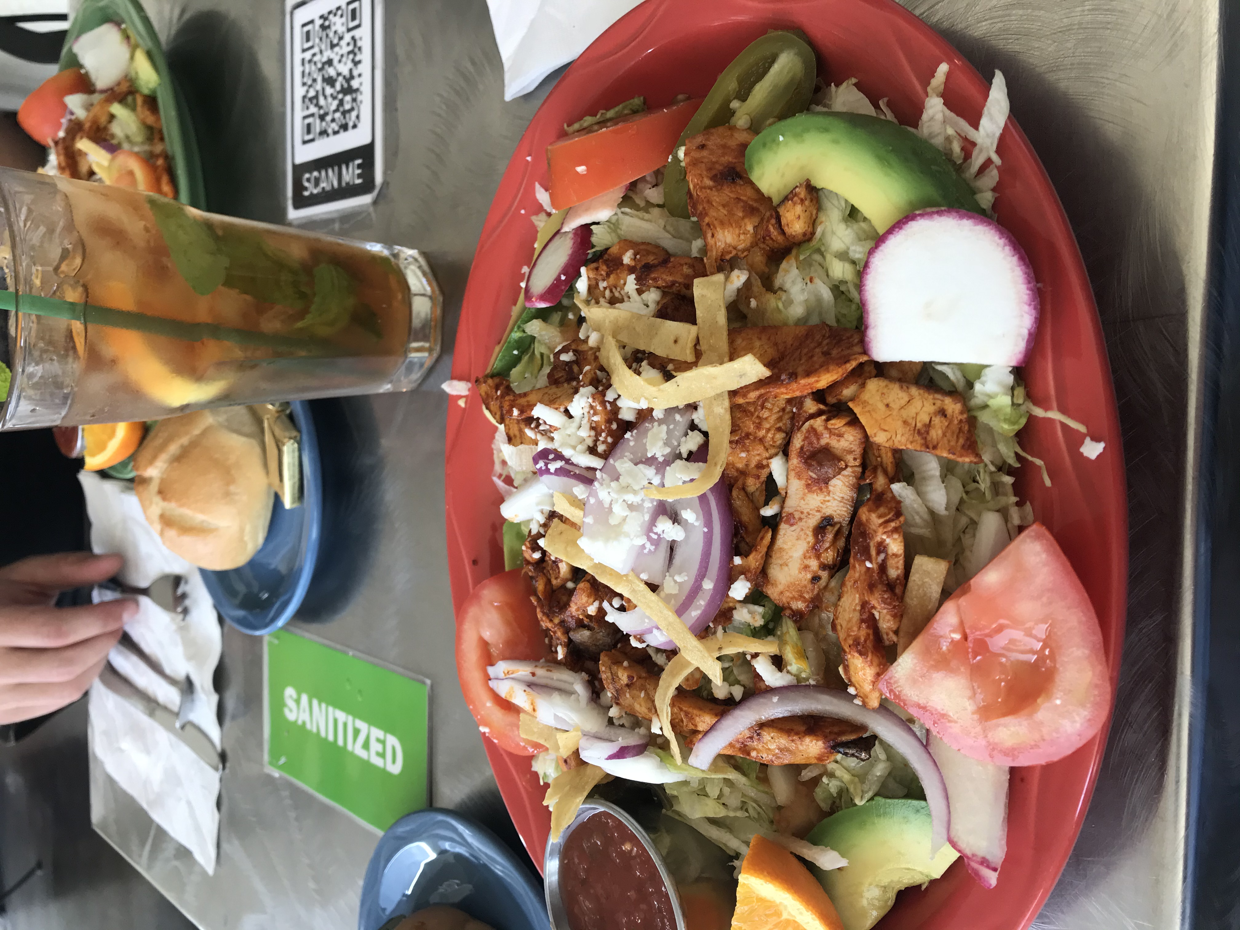 A restaurant salad on a red plate topped with shredded iceberg lettuce, chicken, avocado, and vegetables.