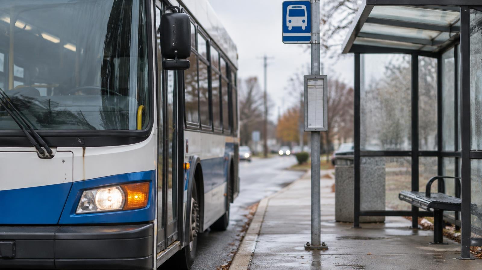 A transit bus stopped at a covered bus shelter beside a route sign.