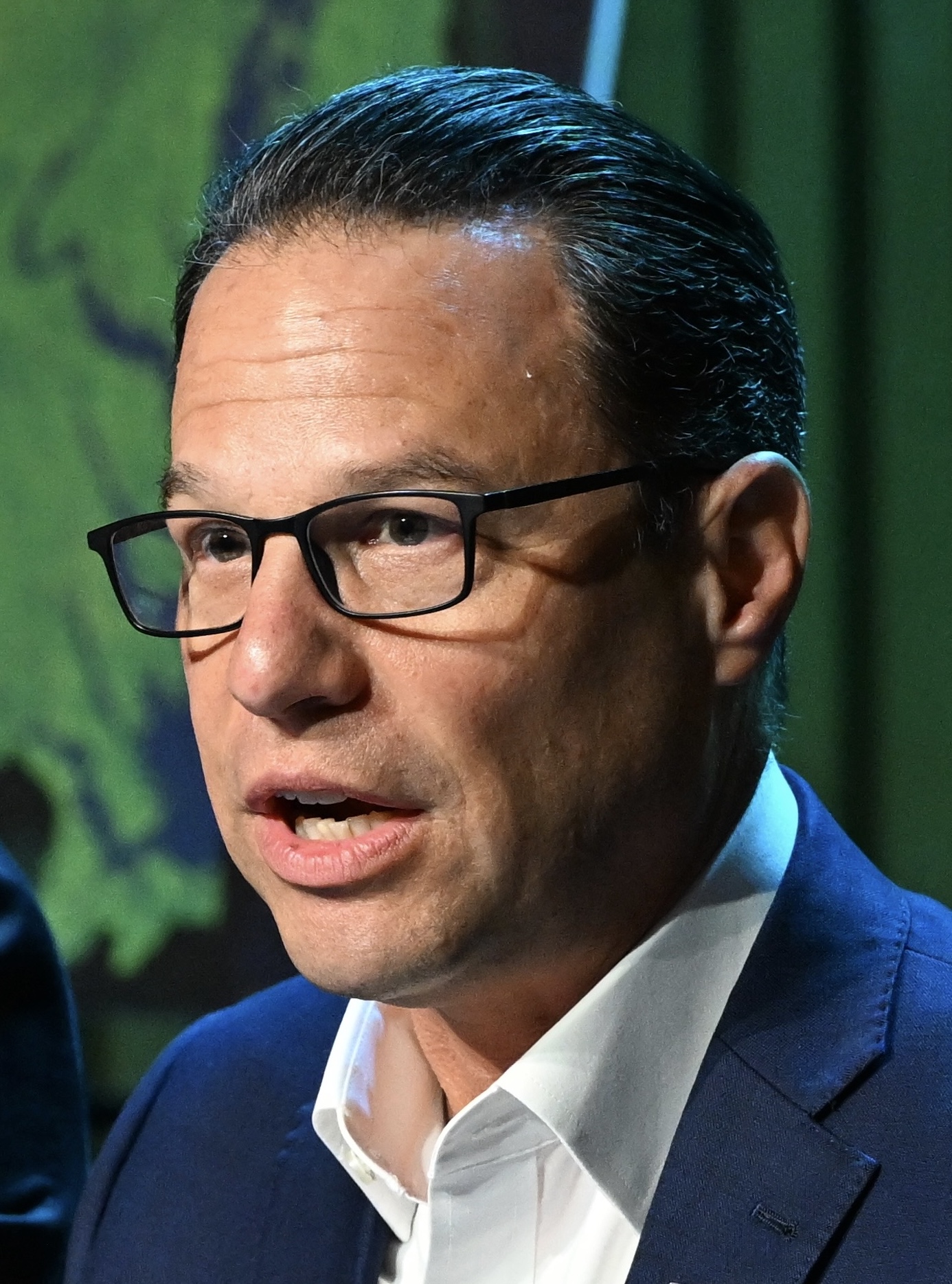 Man in blue suit and black-rimmed glasses speaking at a podium.
