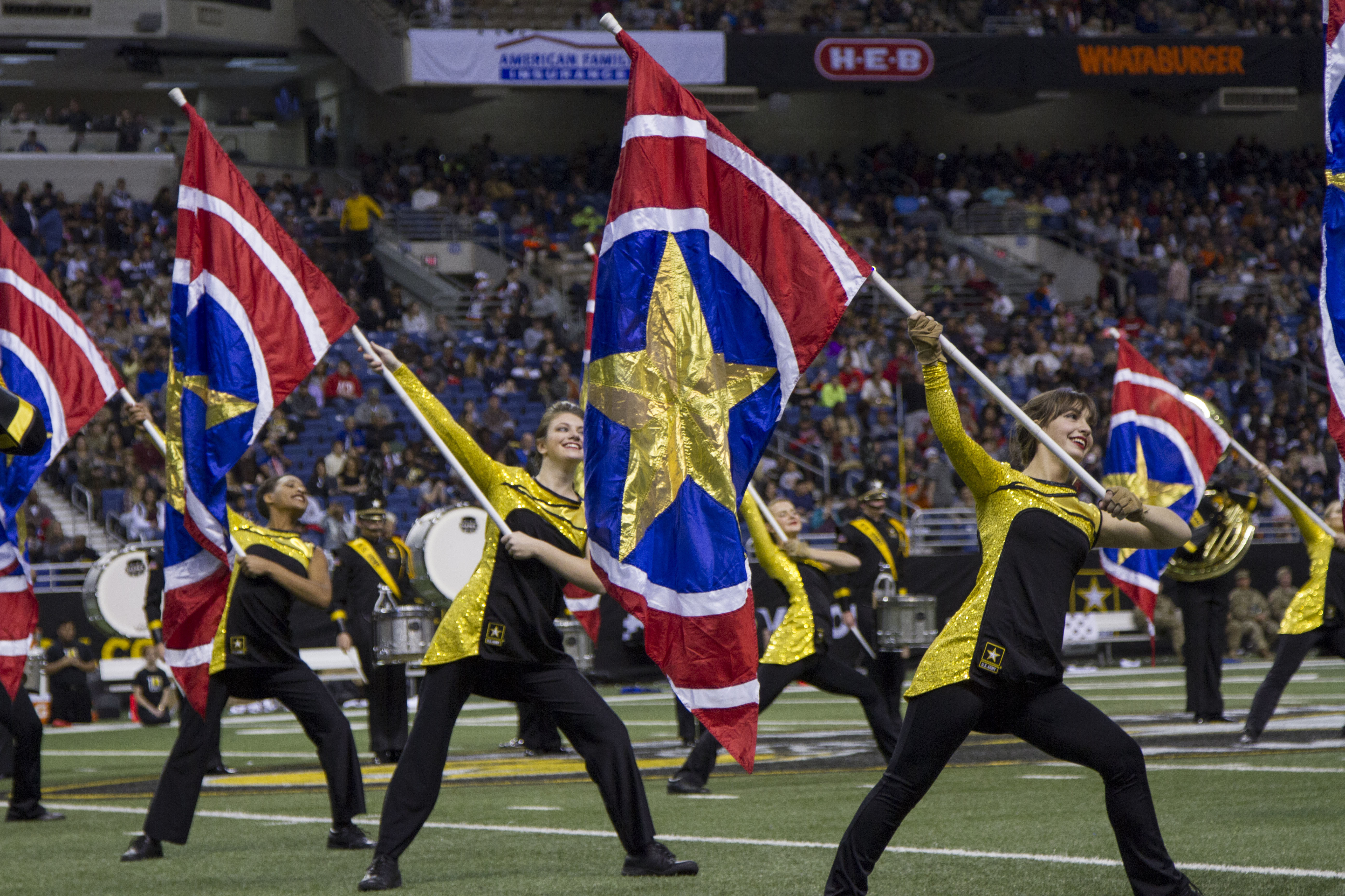 Color guard performers wave large red, white, and blue flags on a football field.