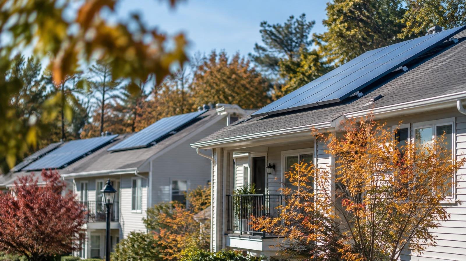 Row of small low-rise apartment buildings with solar panels on rooftops amid trees.