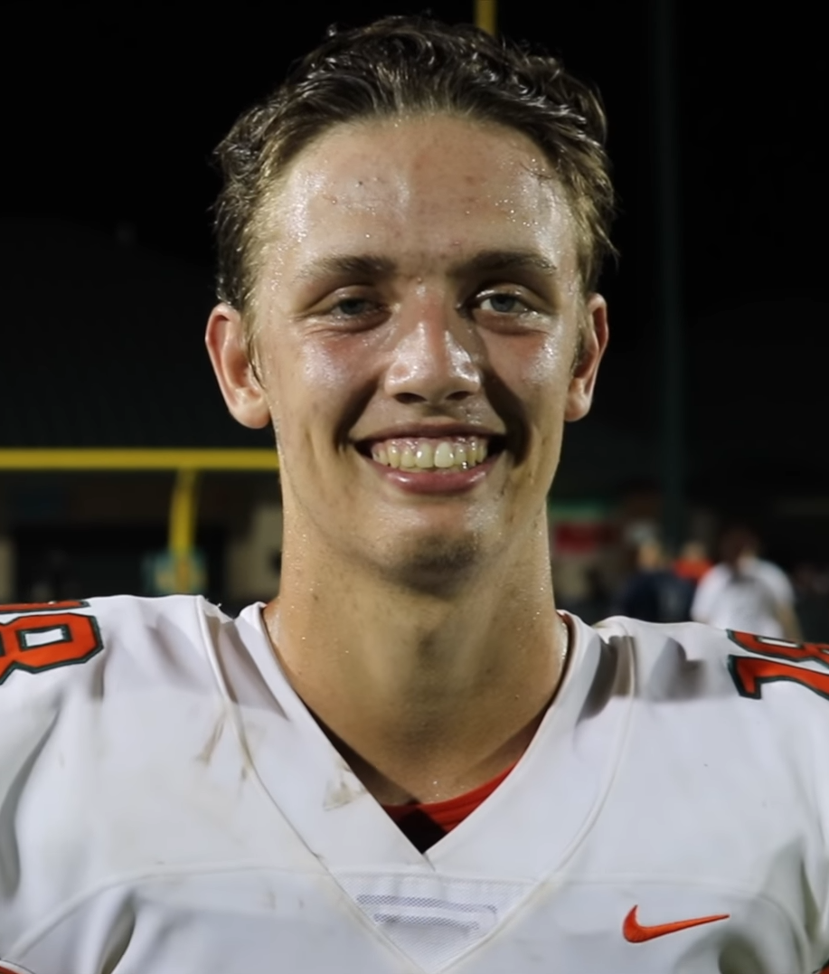 A football player in a white jersey with orange trim and number 16 under stadium lights.