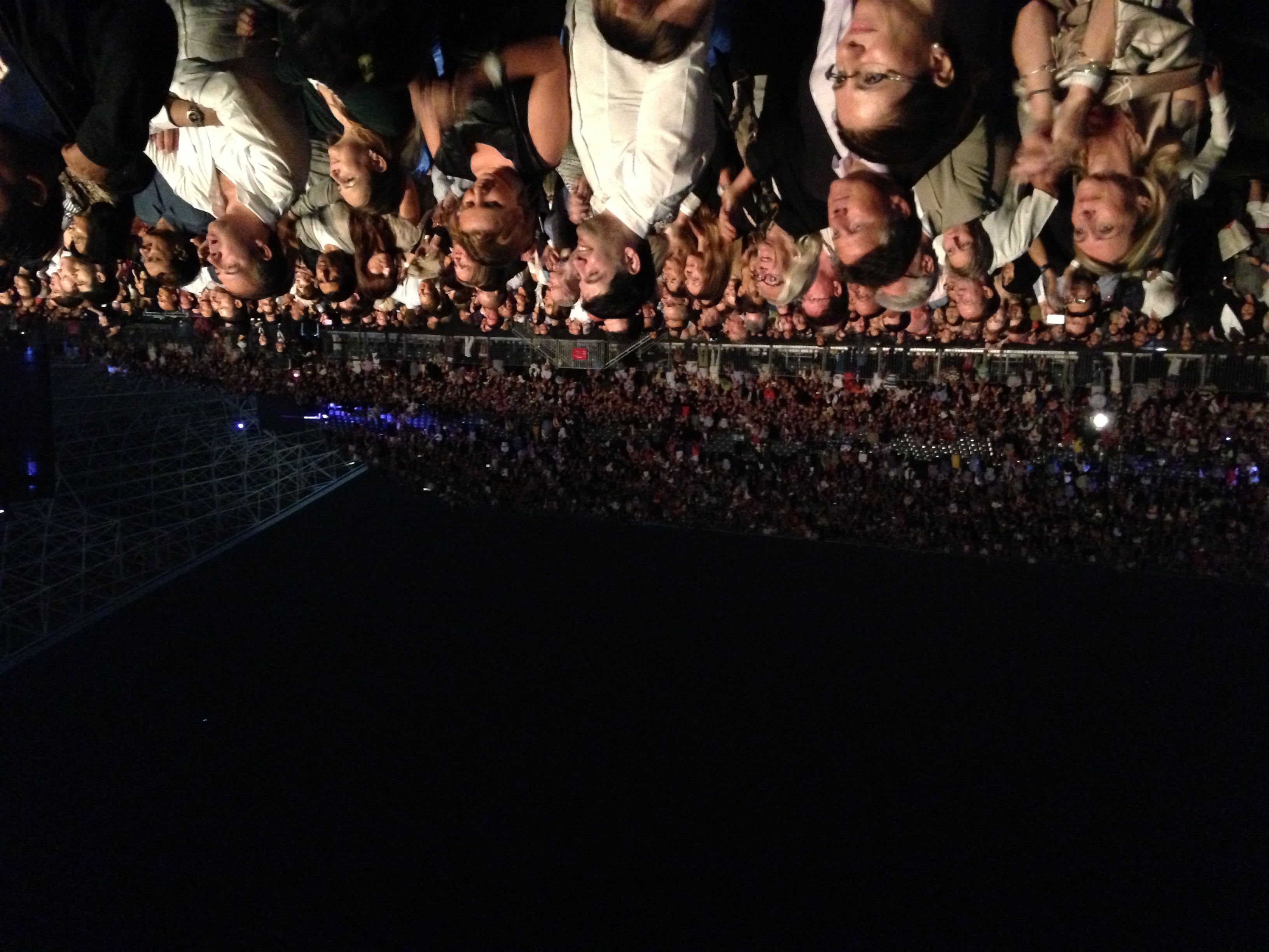 Large crowd standing and applauding at an outdoor amphitheater concert at night.