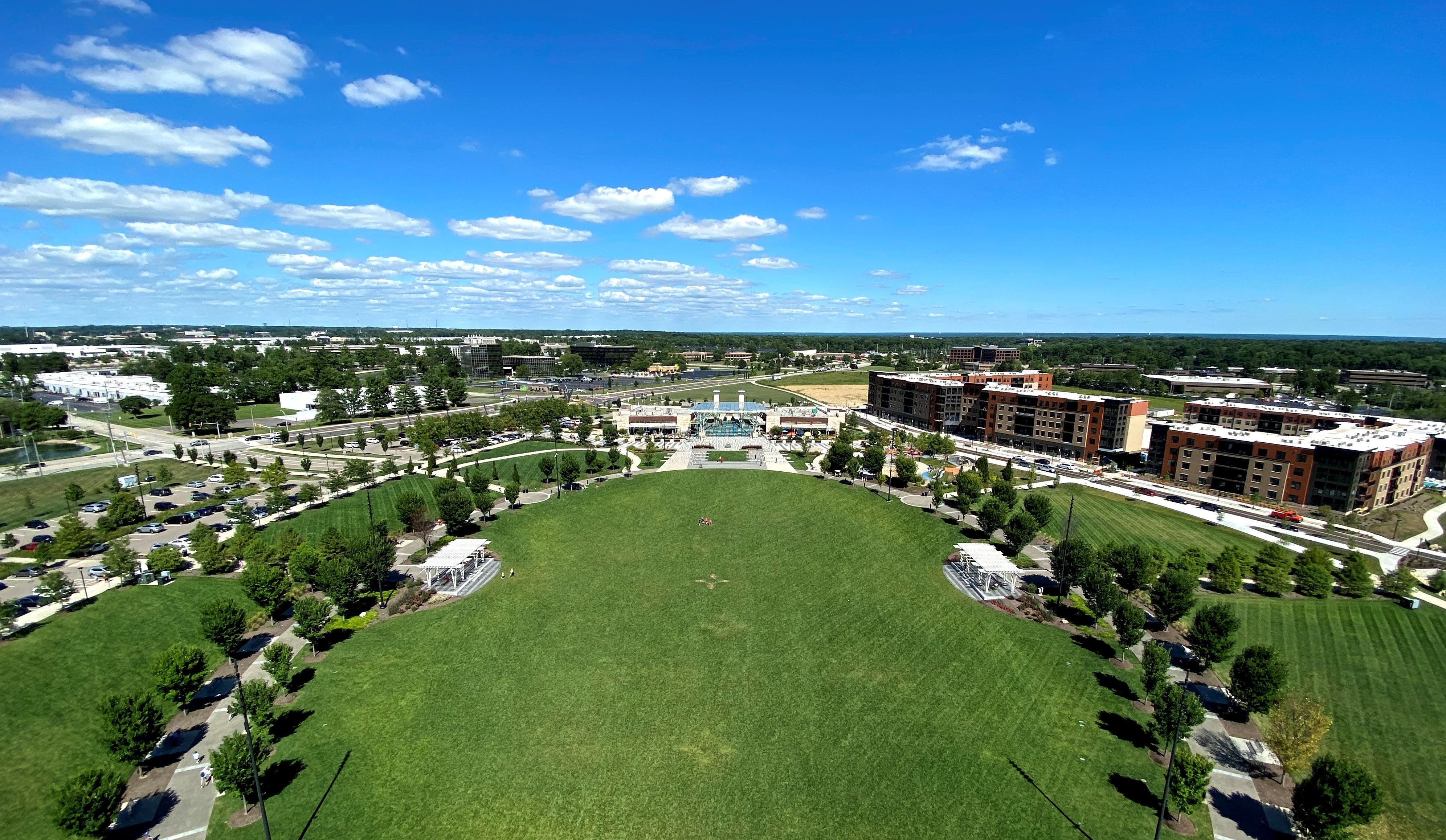 Aerial view of a large green lawn at a park with surrounding buildings and tree-lined paths.