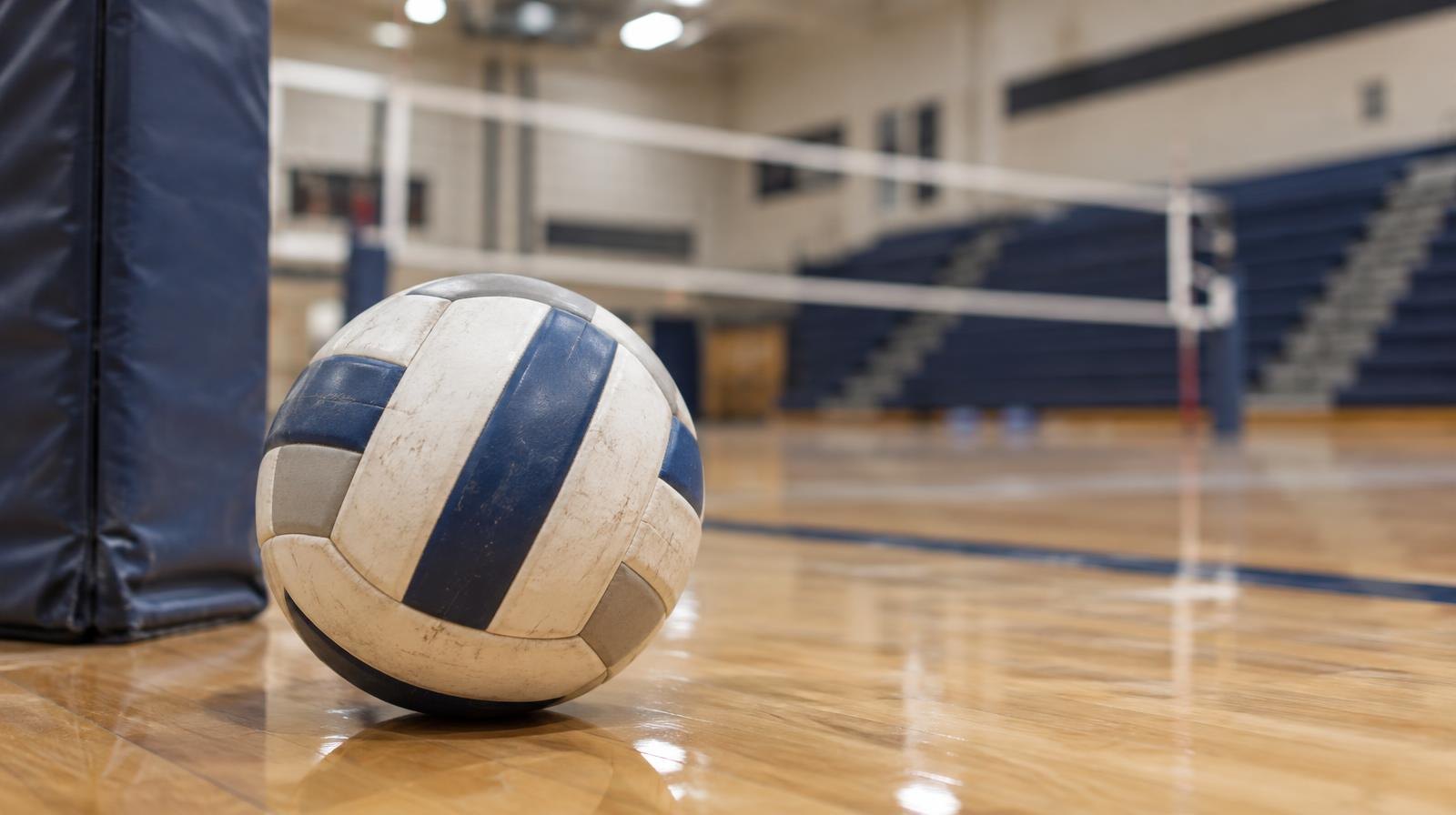 A volleyball resting on a hardwood gymnasium floor near the net post.