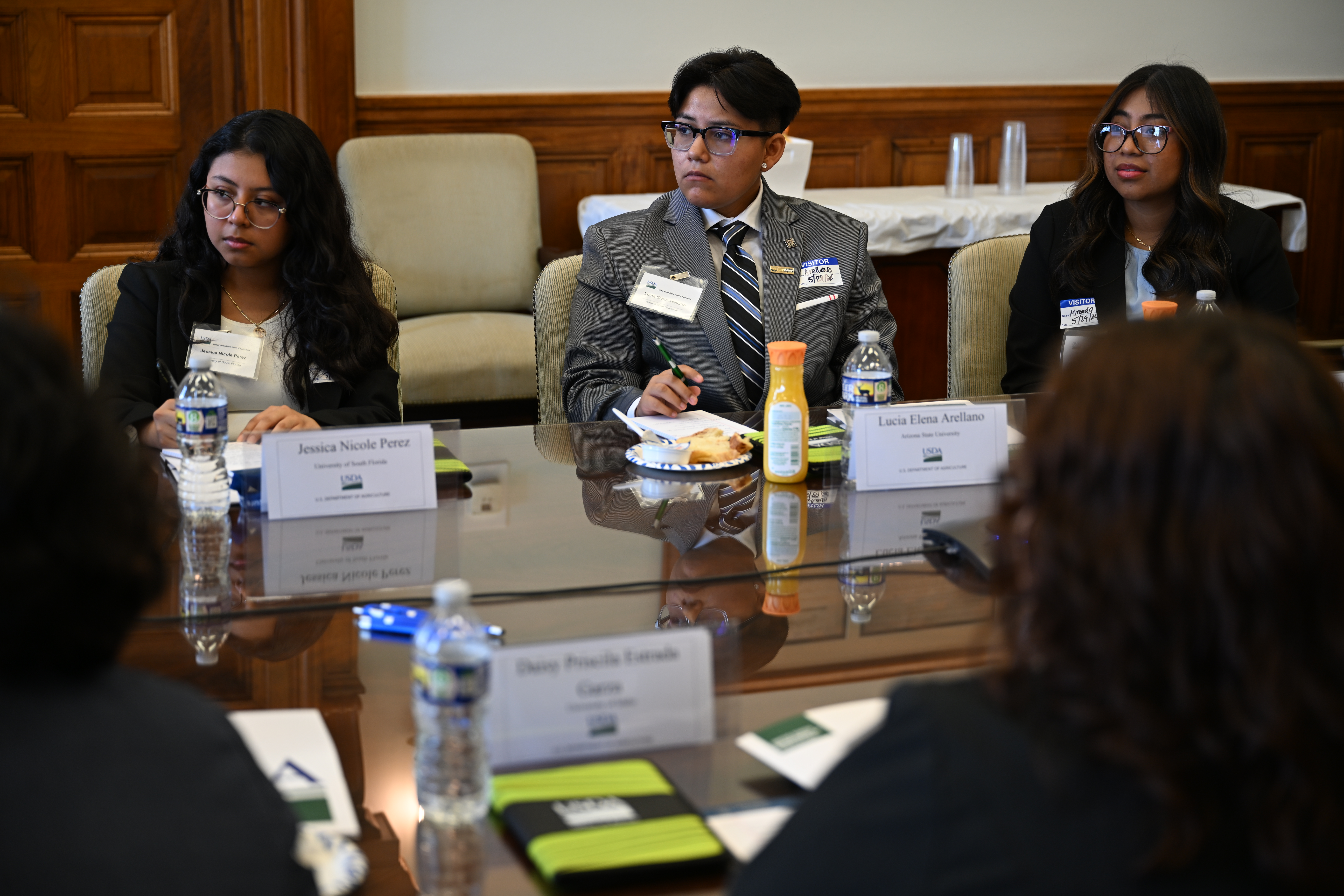Three young people wearing name badges sit at a conference table during an internship orientation.