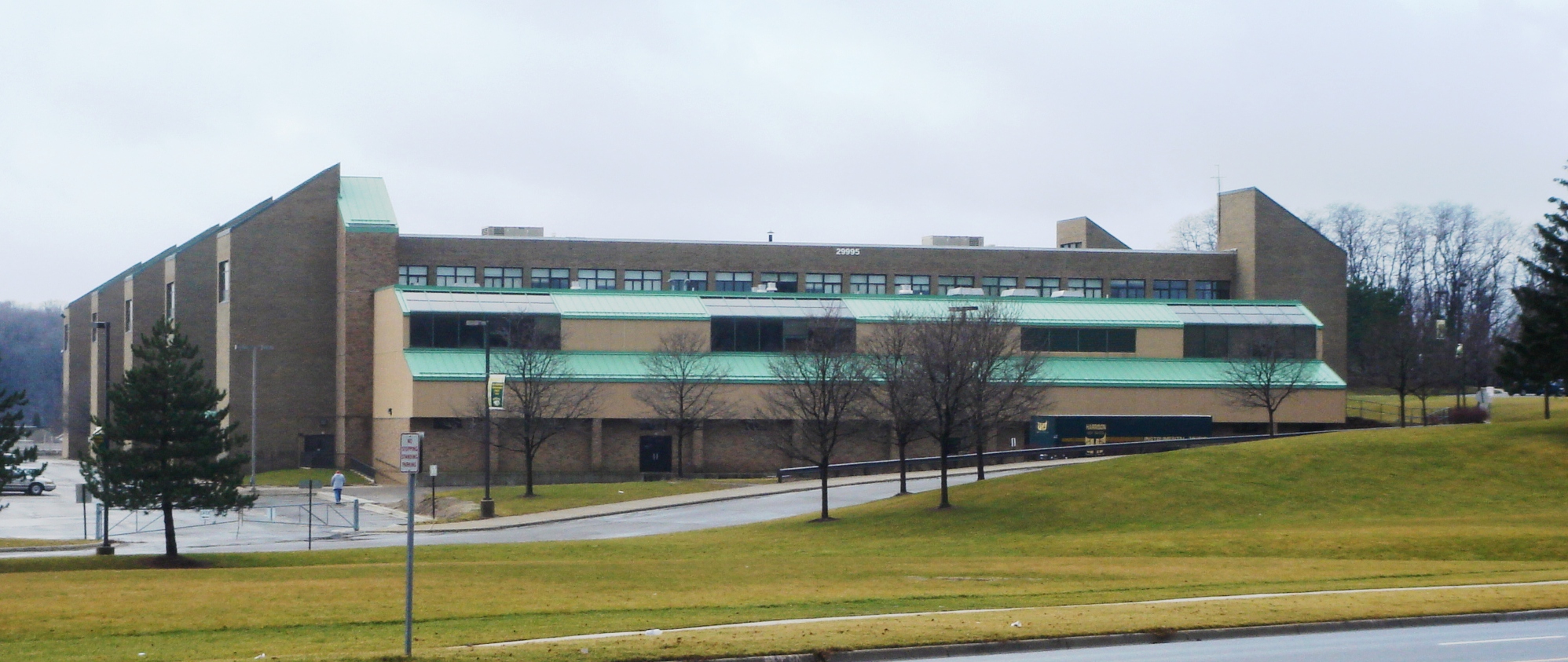 Multi-story brick school building with green window trim and a curved driveway in front.