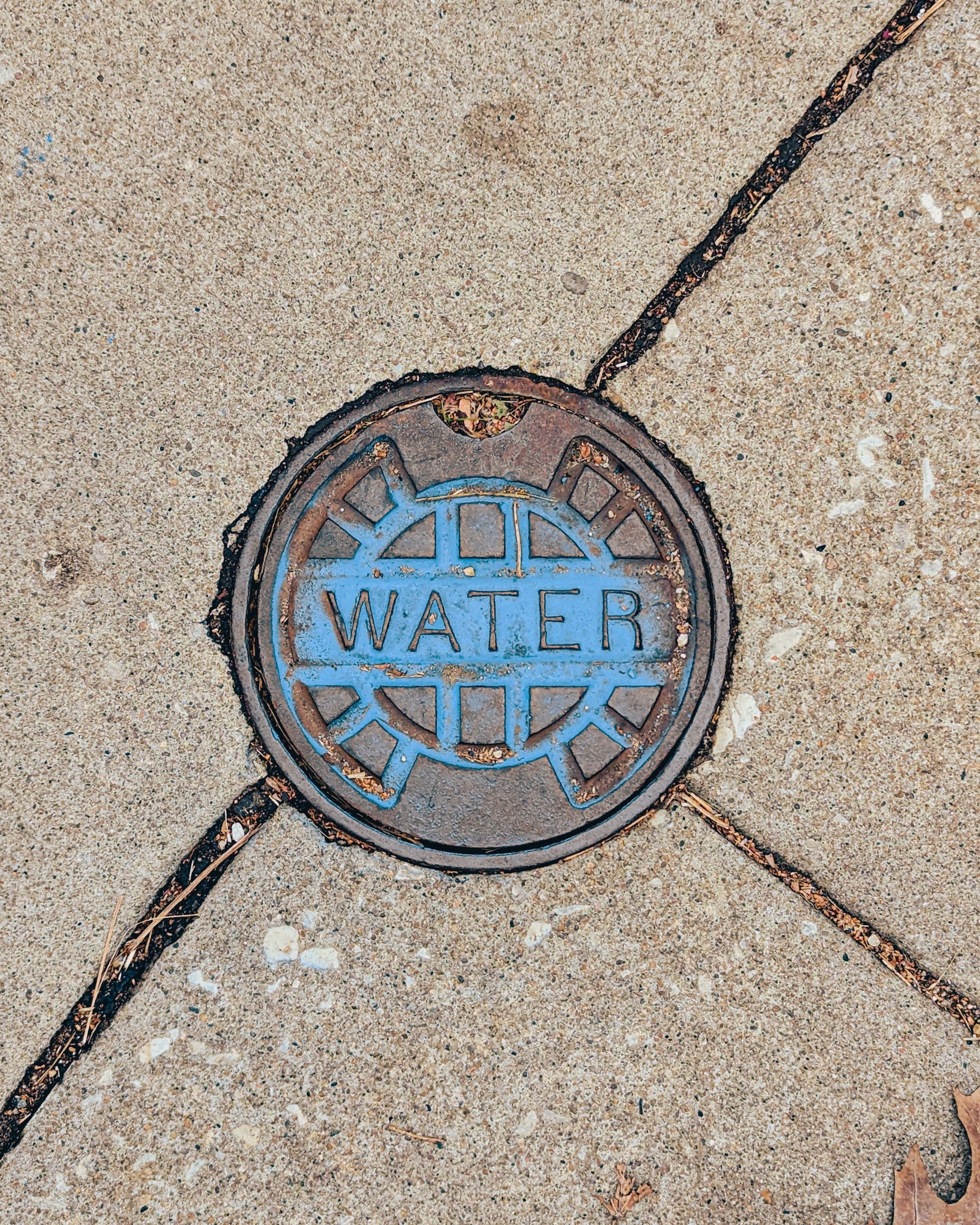 A close-up photo of a metal water cover embedded in a concrete sidewalk, marked with 'water.'