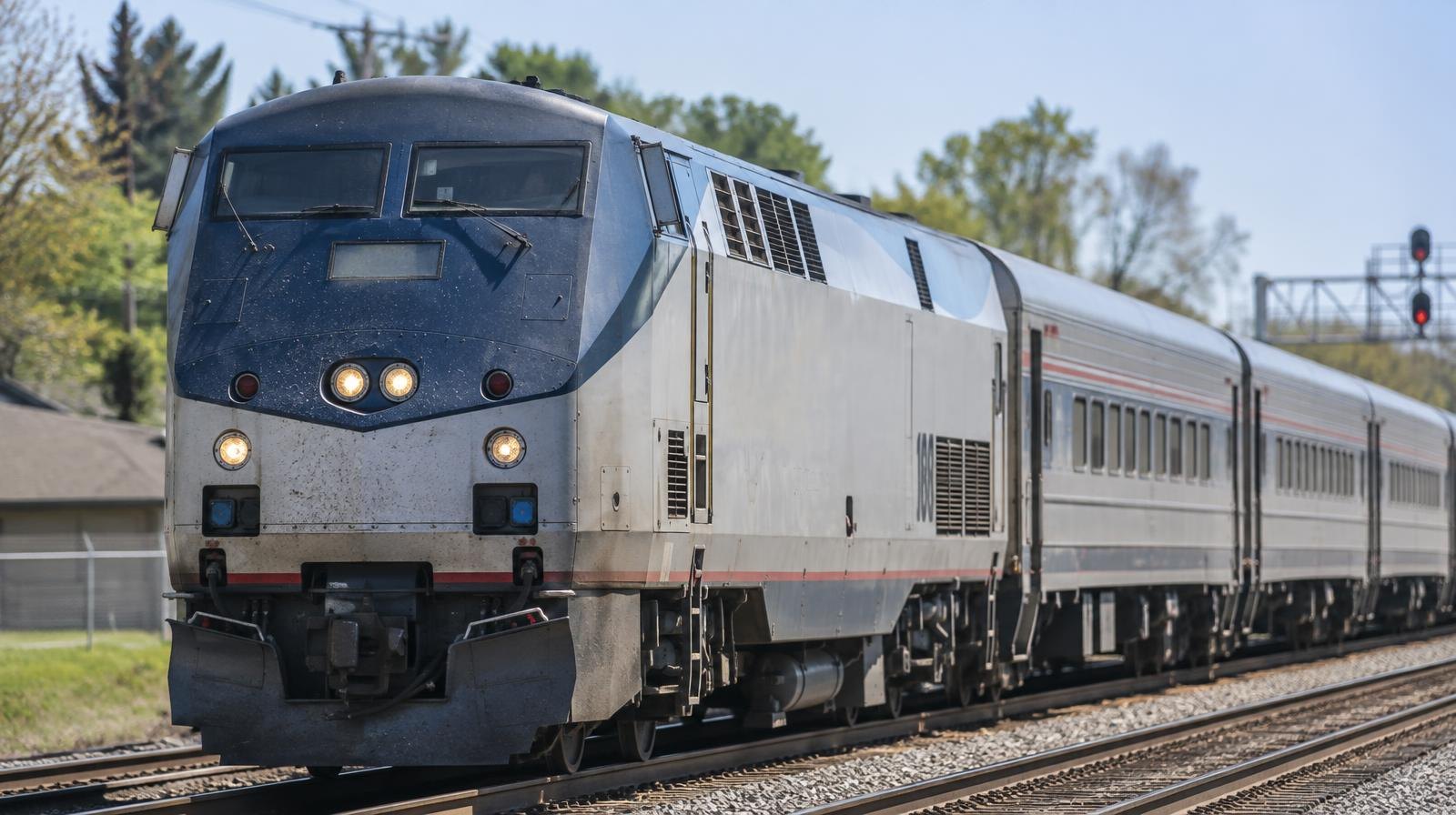 A commuter rail train moves along two parallel tracks through a suburban landscape.