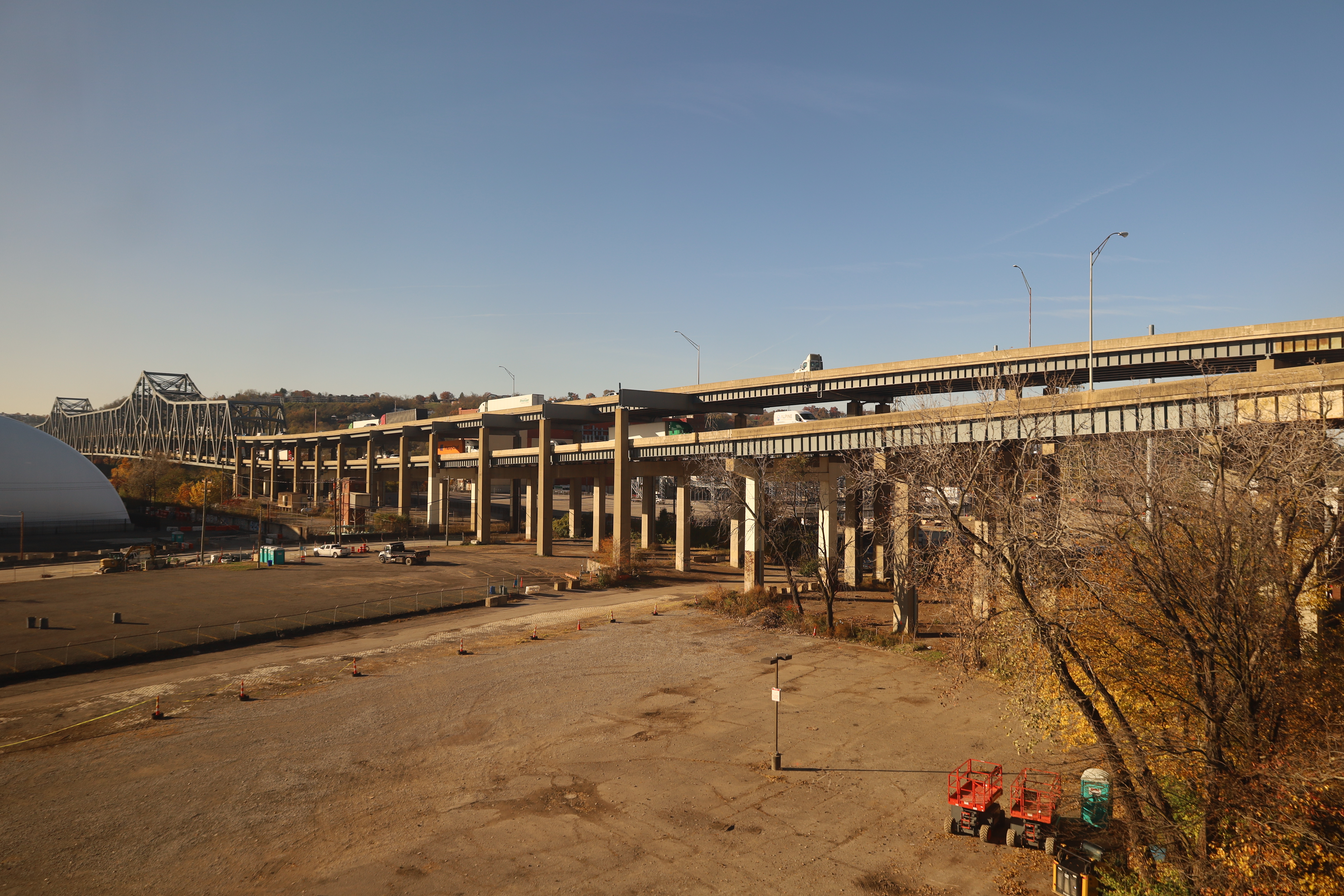 Elevated concrete highway columns and spans near a steel truss bridge, autumn foliage visible.