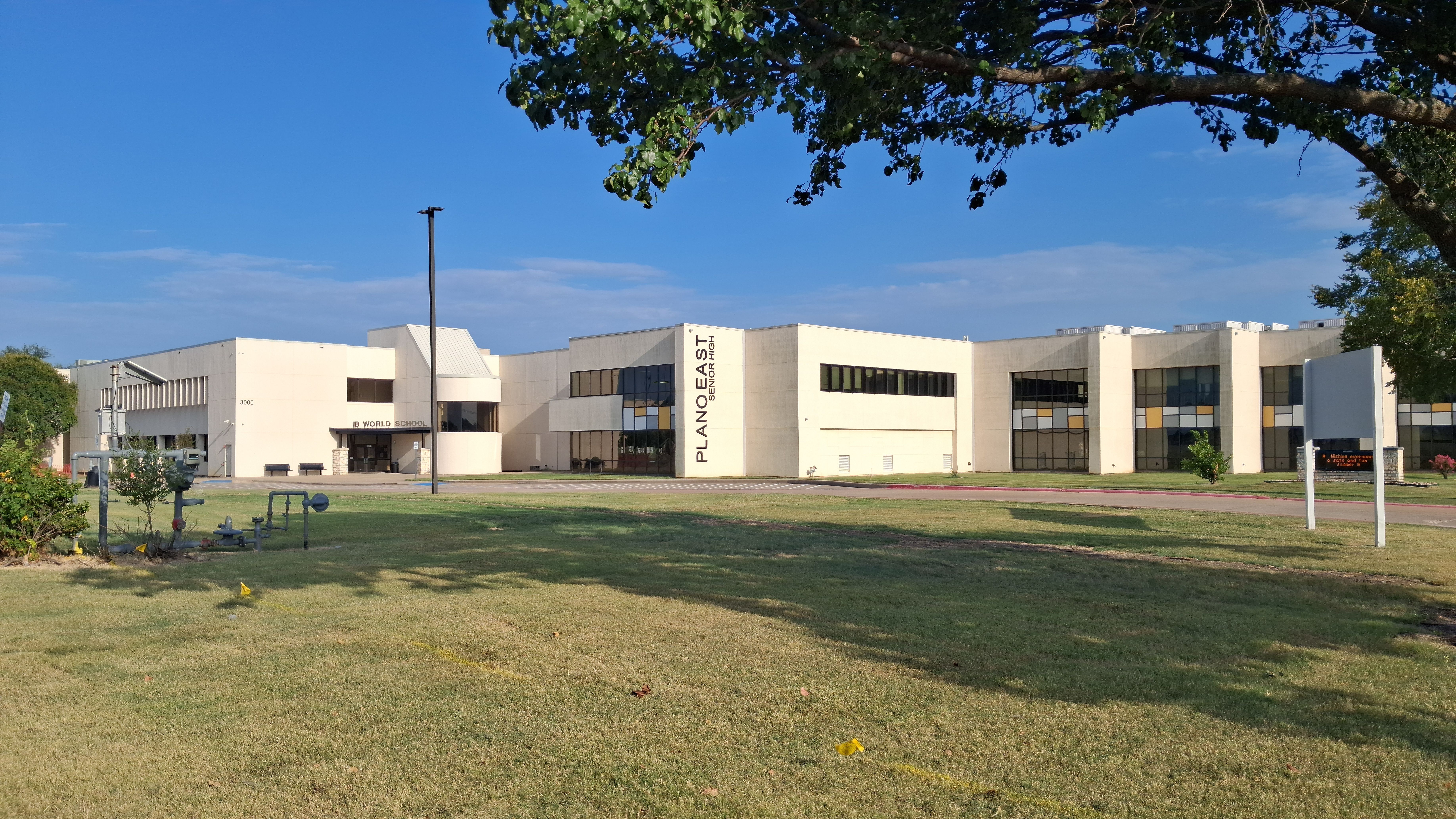 Large low-rise school building with 'Plano East' signage on facade, green lawn in front.
