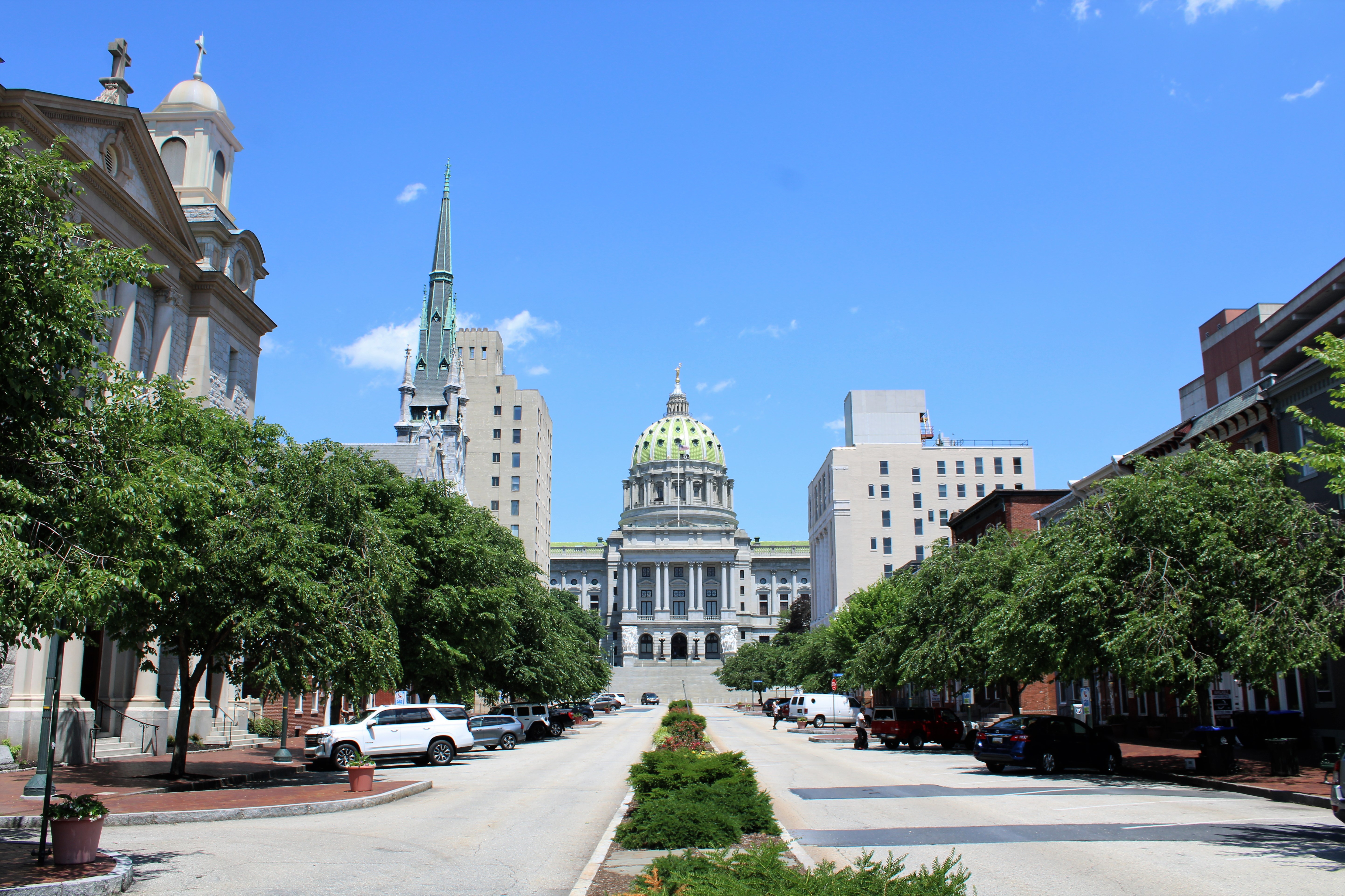 Tree-lined street leading toward the Pennsylvania State Capitol dome on a sunny day.