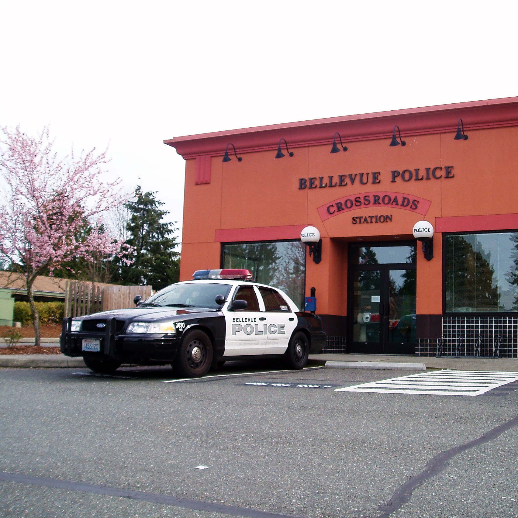 Black-and-white police patrol car parked outside an orange station building.