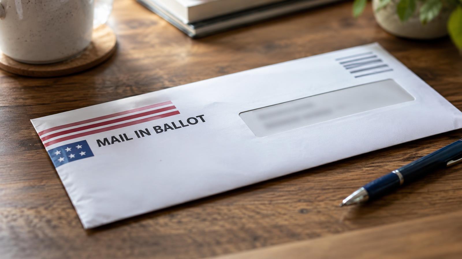 A sealed official mail-in ballot envelope on a wooden surface next to a pen.