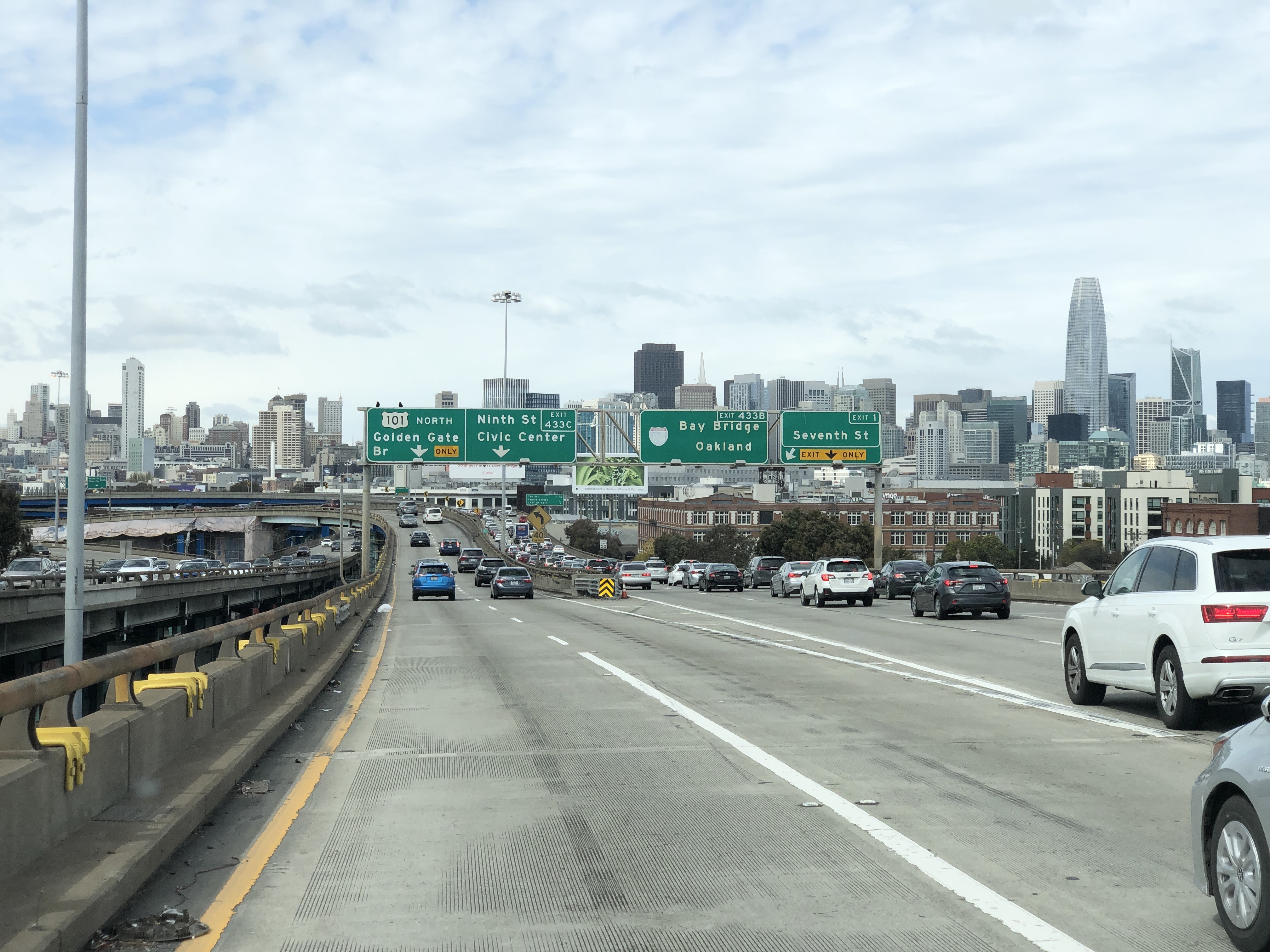 Multi-lane urban freeway with overhead green highway signs pointing toward the Bay Bridge.