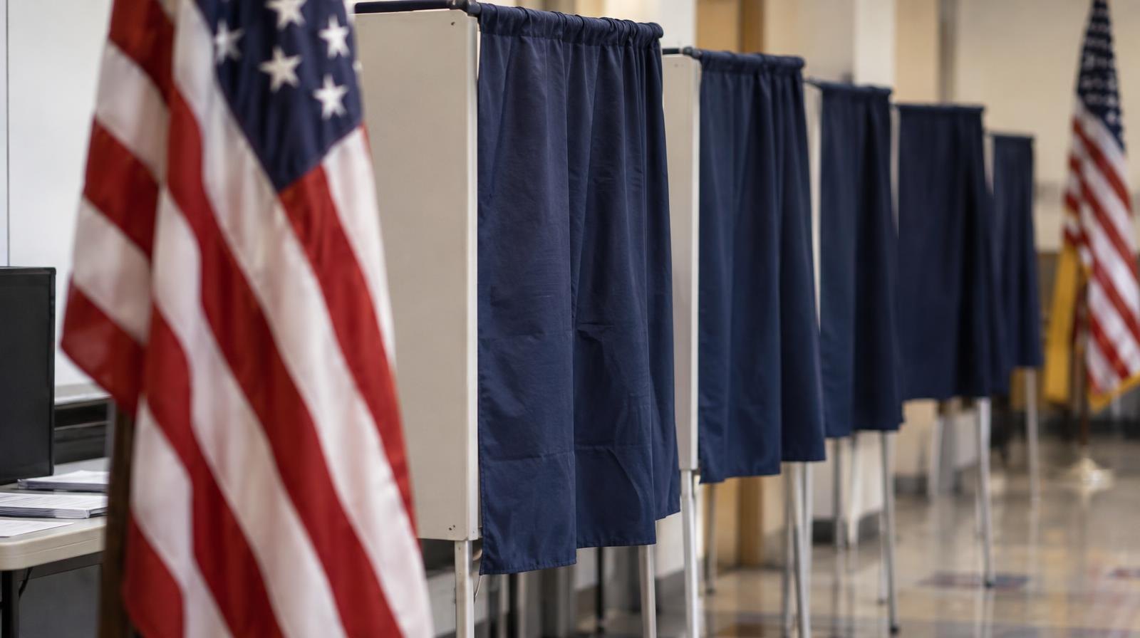 A row of empty voting booths with privacy curtains inside a polling place.