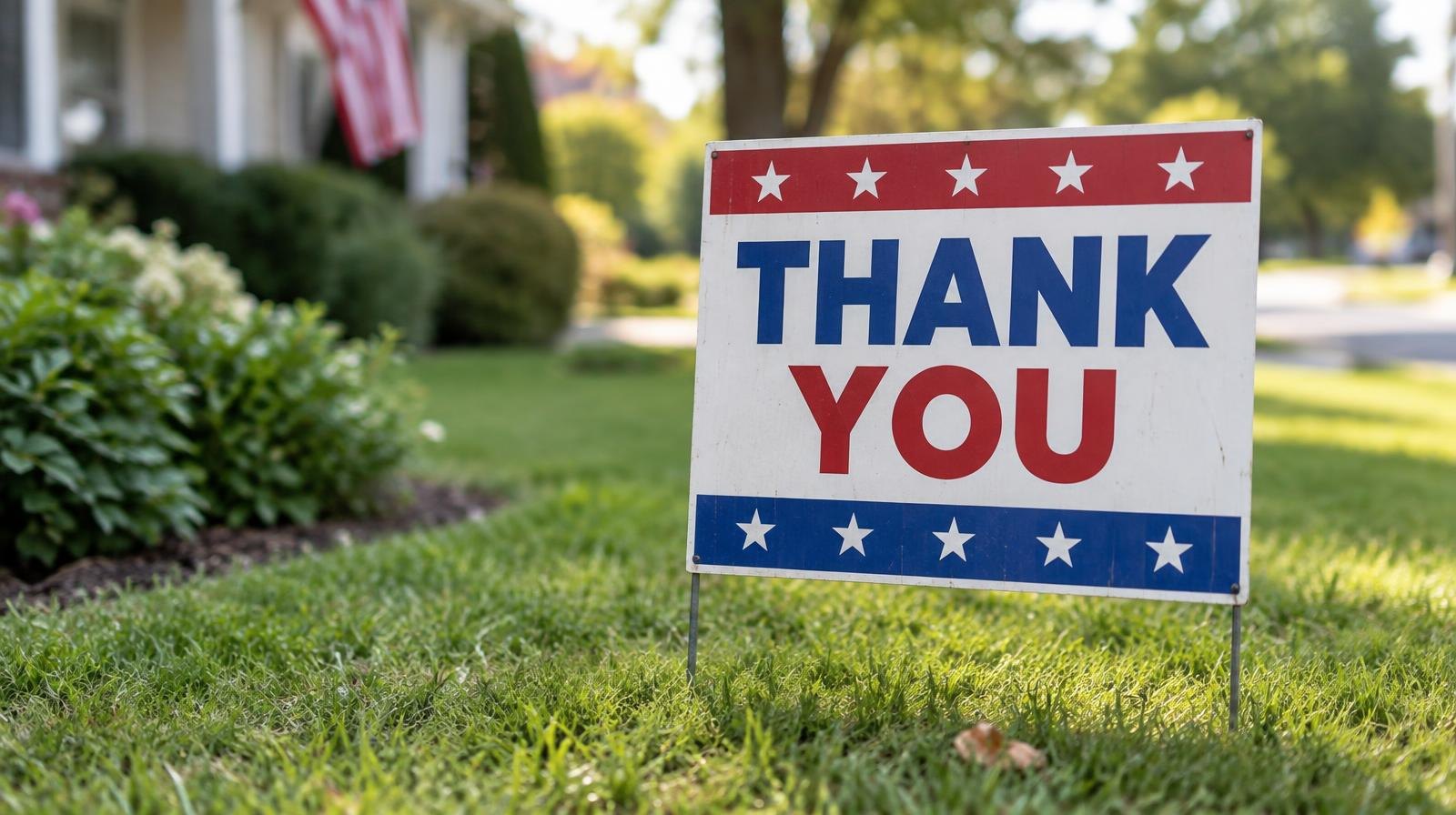 Small patriotic yard sign with red, white, and blue colors in a green lawn.