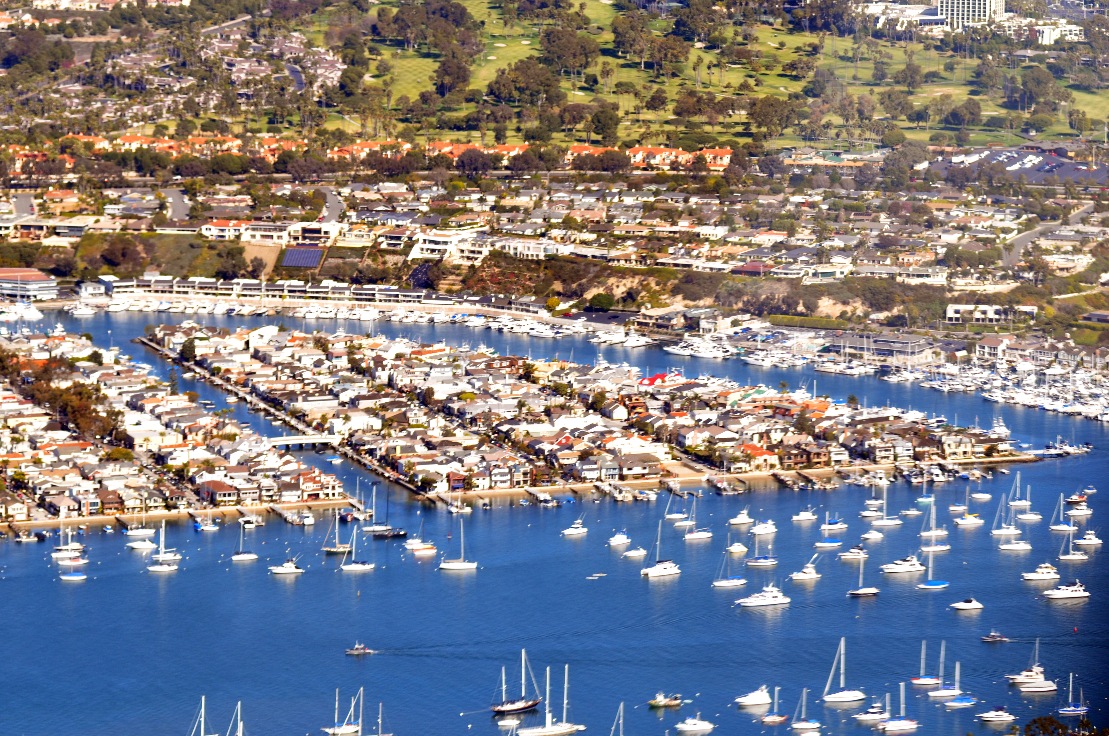 Aerial view of a small island with waterfront homes, docks, and sailboats in a harbor.