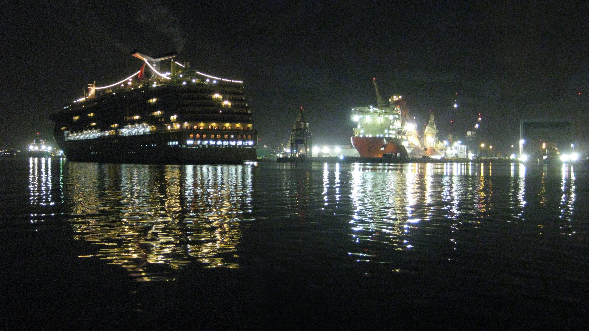 The MS Carnival Legend enters the Port of Tampa's Sparkman Channel in the darkness of the early Florida morning, passing the CSO Deep Blue, which is in drydock at Tampa Ship, LLC.